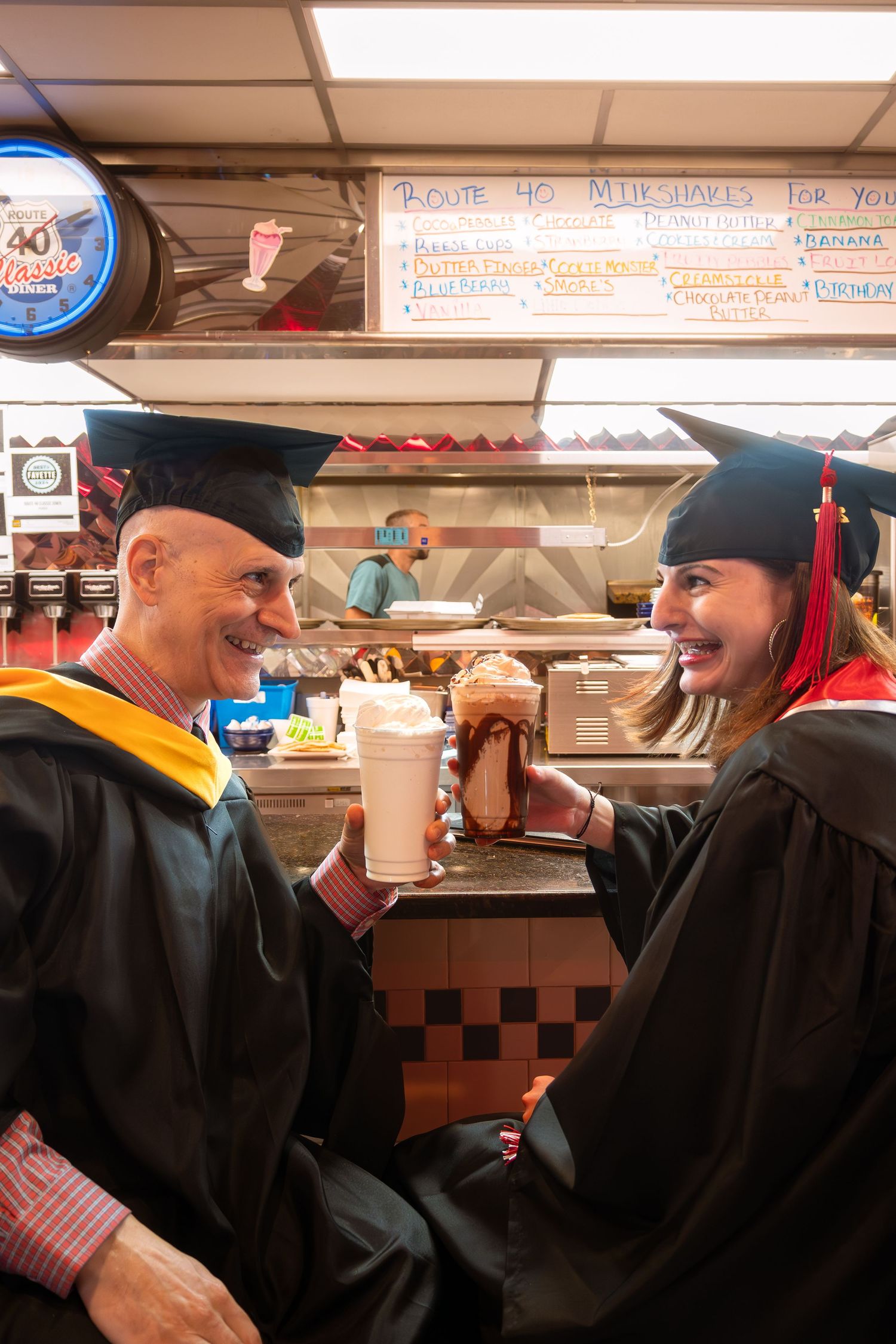Graduates in black caps and gowns celebrate together indoors.