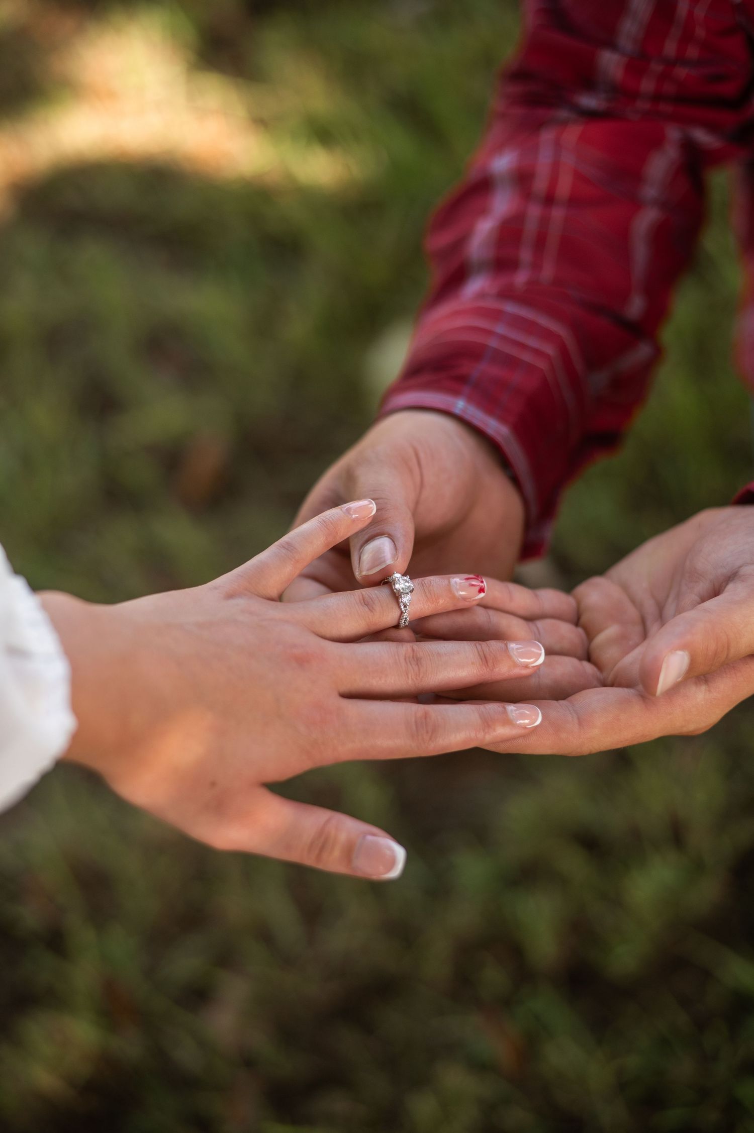 Close-up of hands exchanging an engagement ring outdoors.