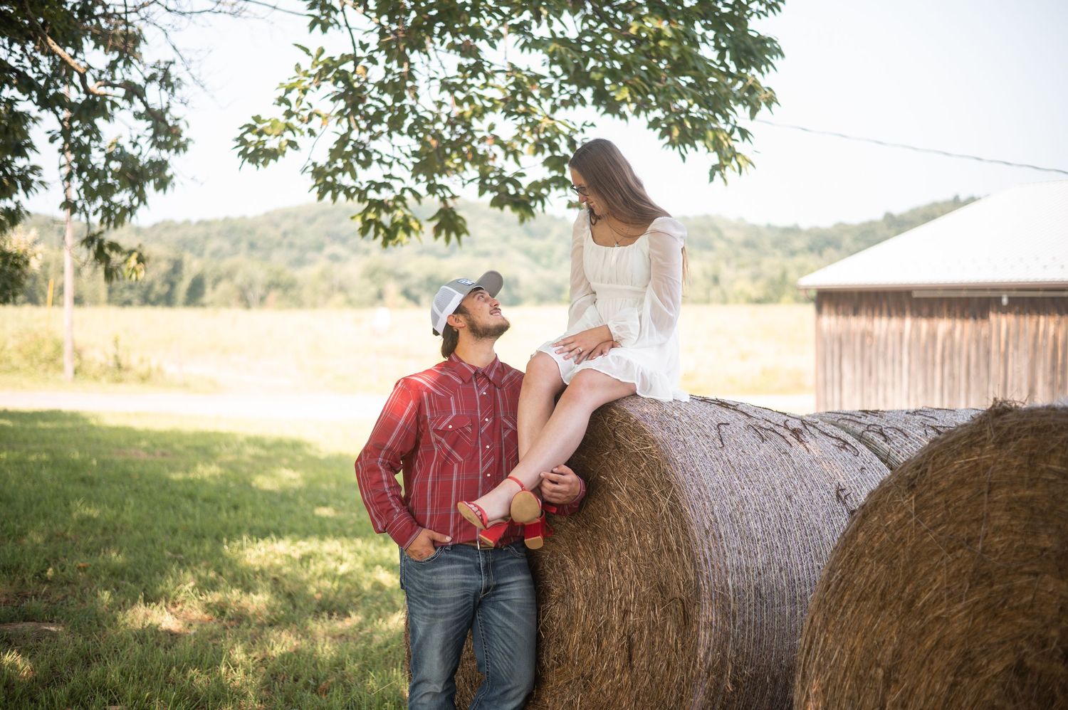 Rustic engagement photo setting with hay bales and natural outdoor lighting.