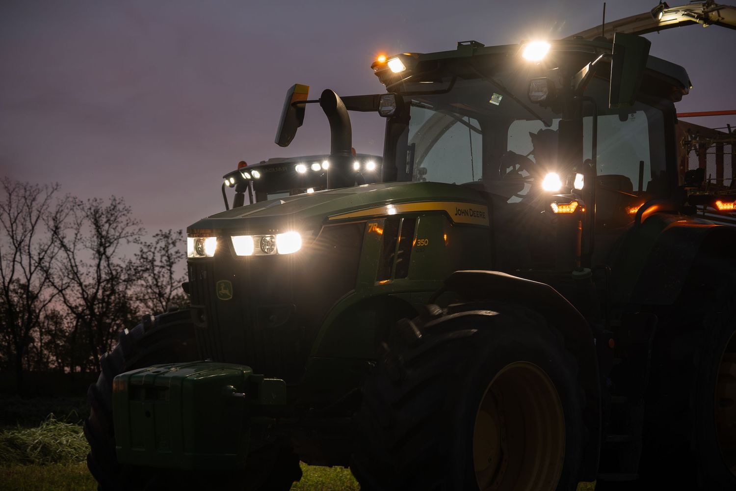 Agricultural tractors working at night with bright headlights illuminating the field.