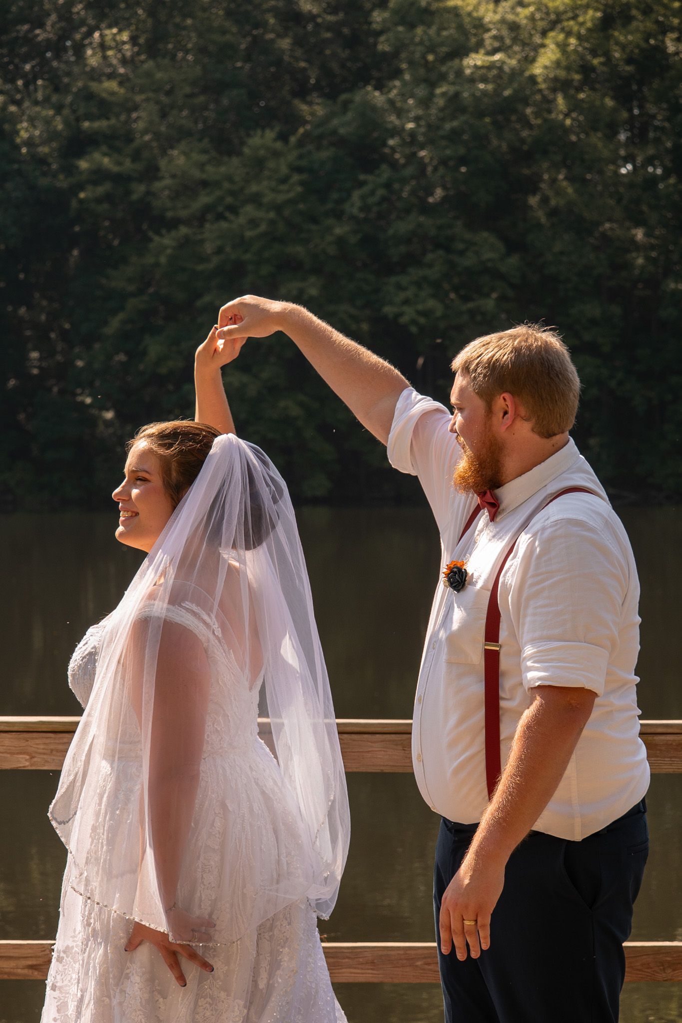 A couple shares a romantic dance moment on a wooden deck overlooking a serene lake during a summer wedding celebration.