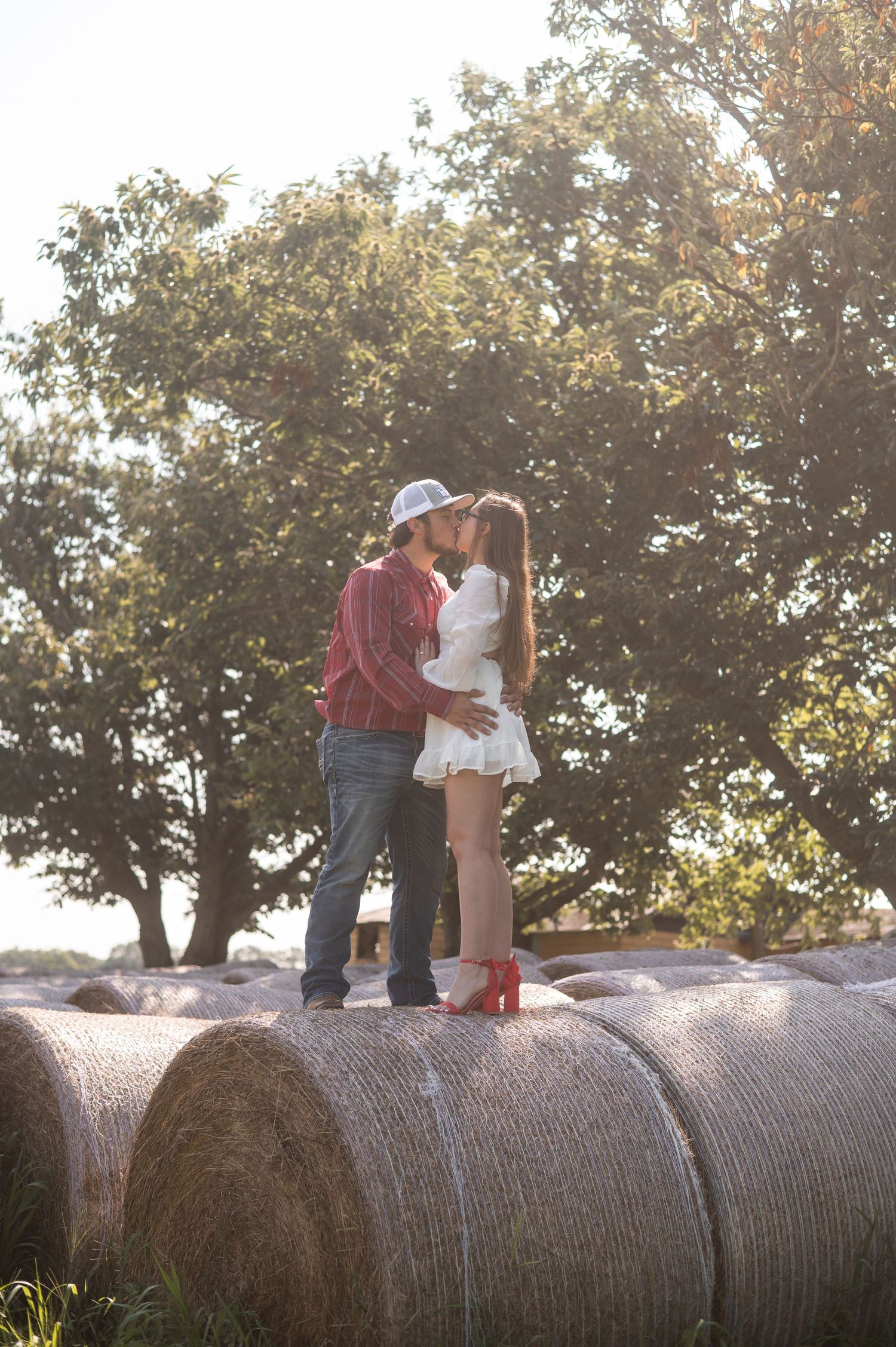A couple shares a romantic moment atop large hay bales during sunset.