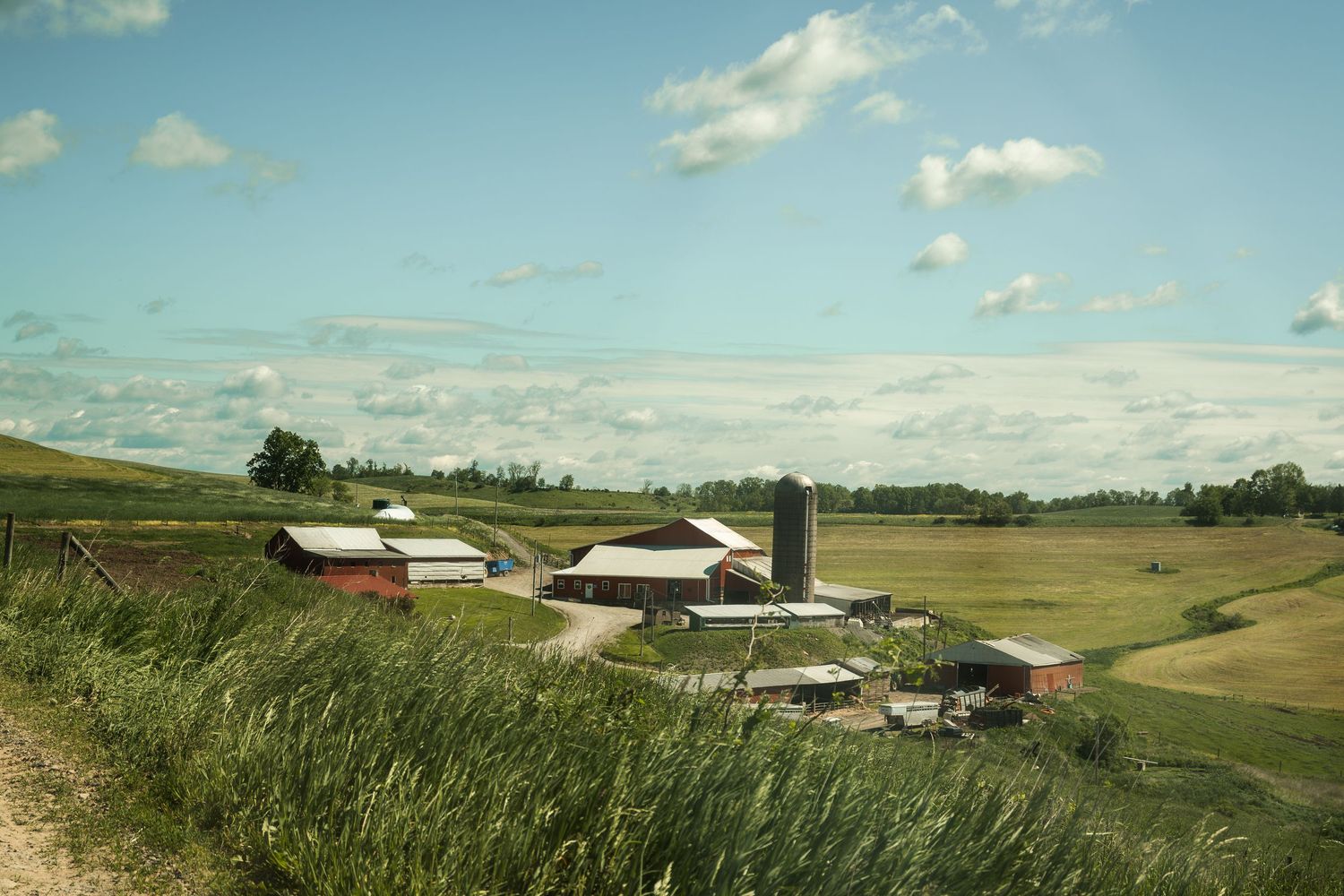 A rural farm panorama shows fields and buildings under a bright blue sky.