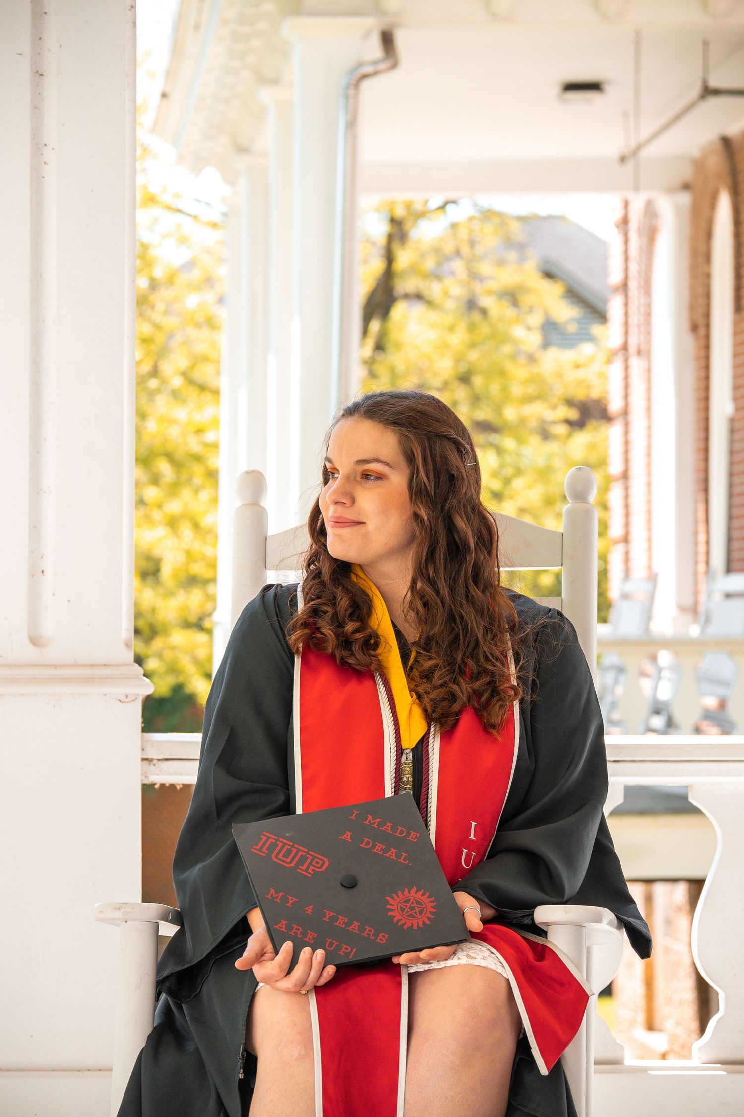Graduate holding decorated cap poses in front of white columns.