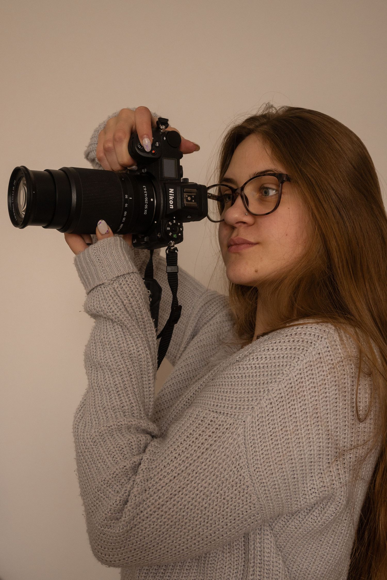 A photographer in a grey sweater holds a professional camera in various poses.