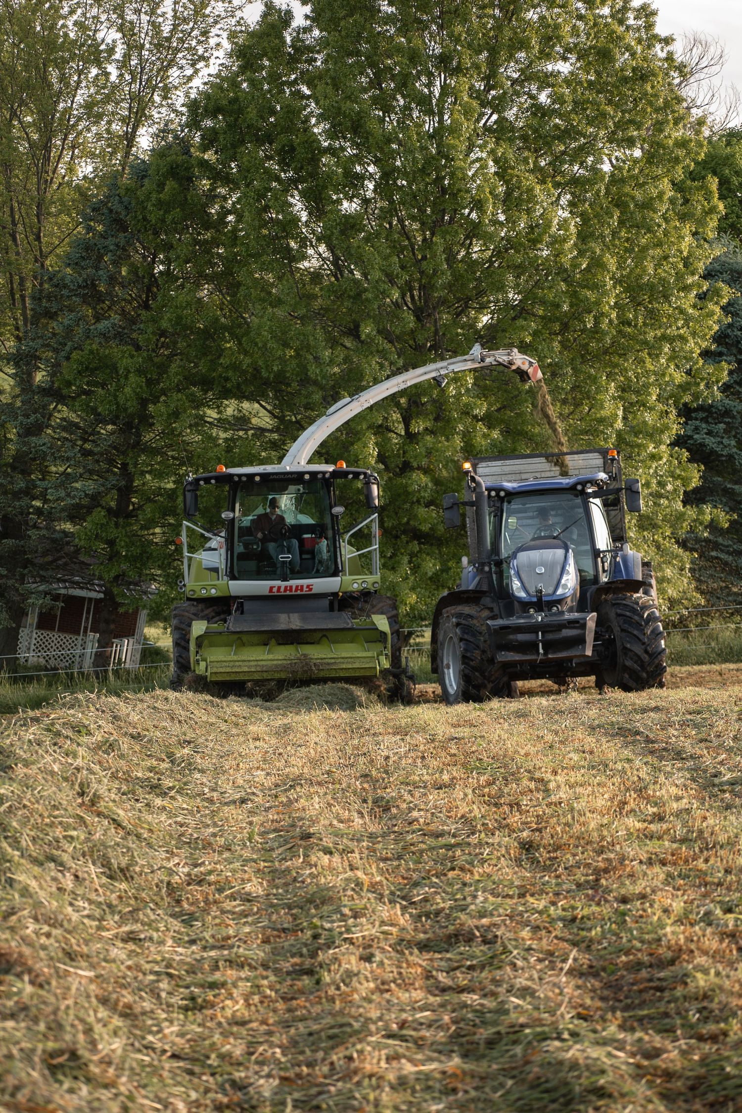 Agricultural machinery working on a hillside with green trees in the background.