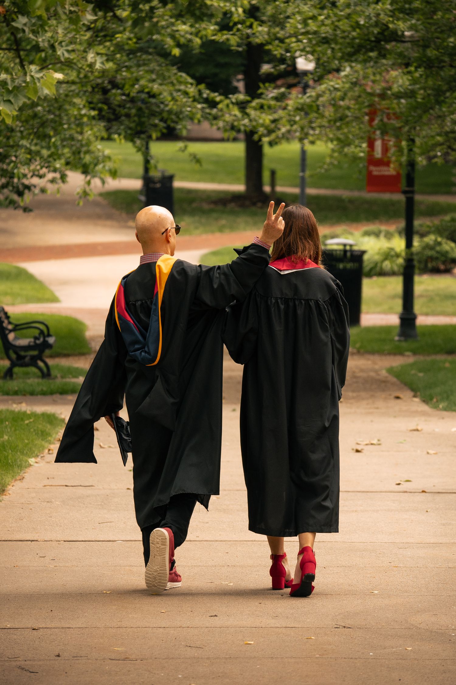 Two graduates in black robes walking together on a park path.