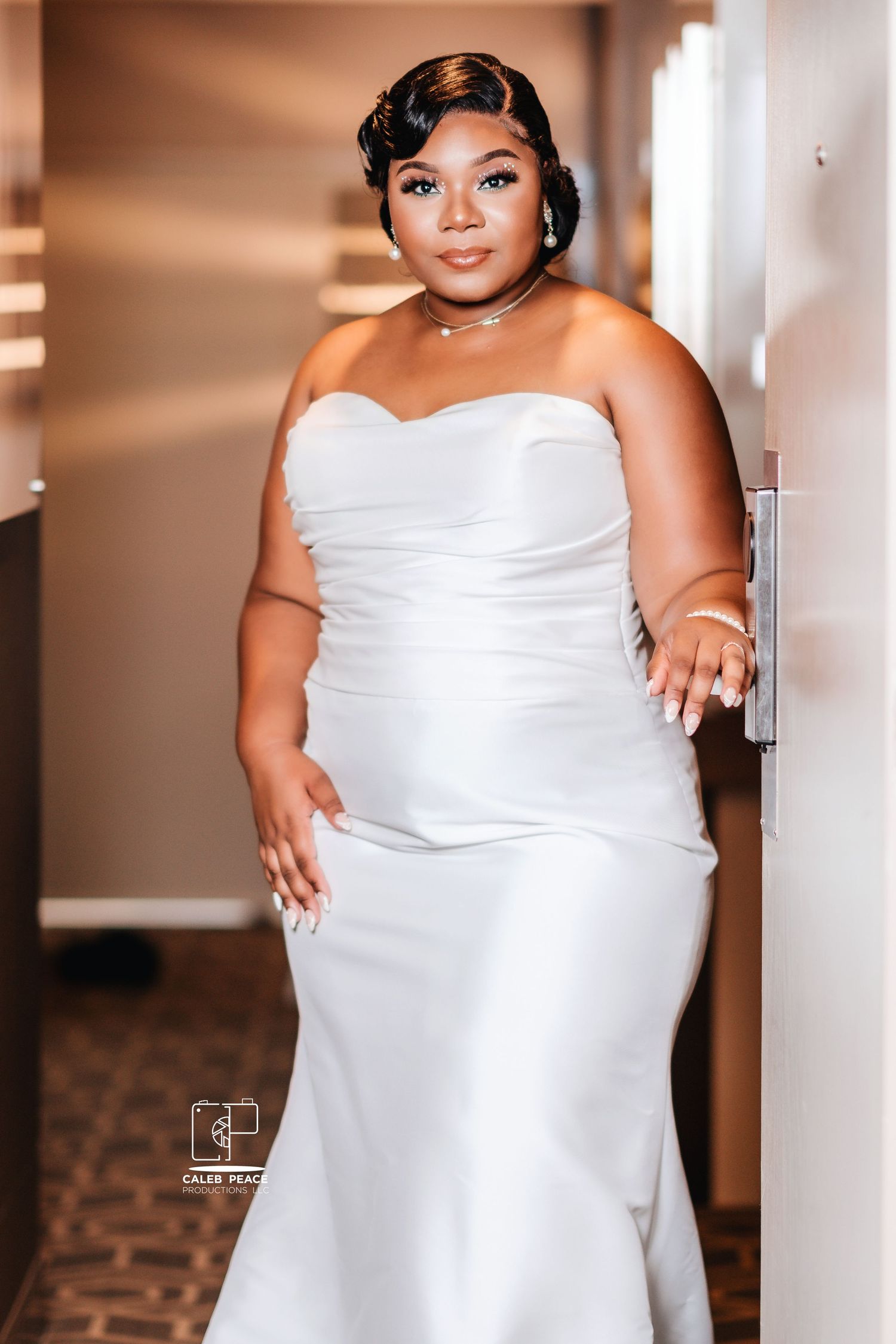 An elegant bride poses in a strapless white wedding gown in an indoor venue with warm lighting.