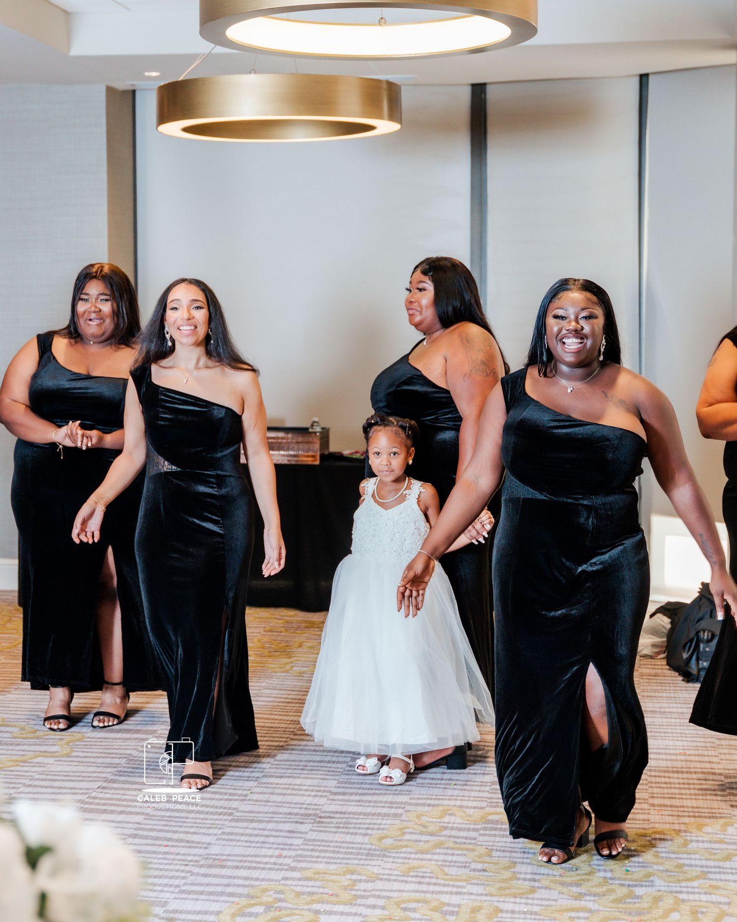 Bridesmaids in black velvet dresses pose with a flower girl in white during wedding party photos.