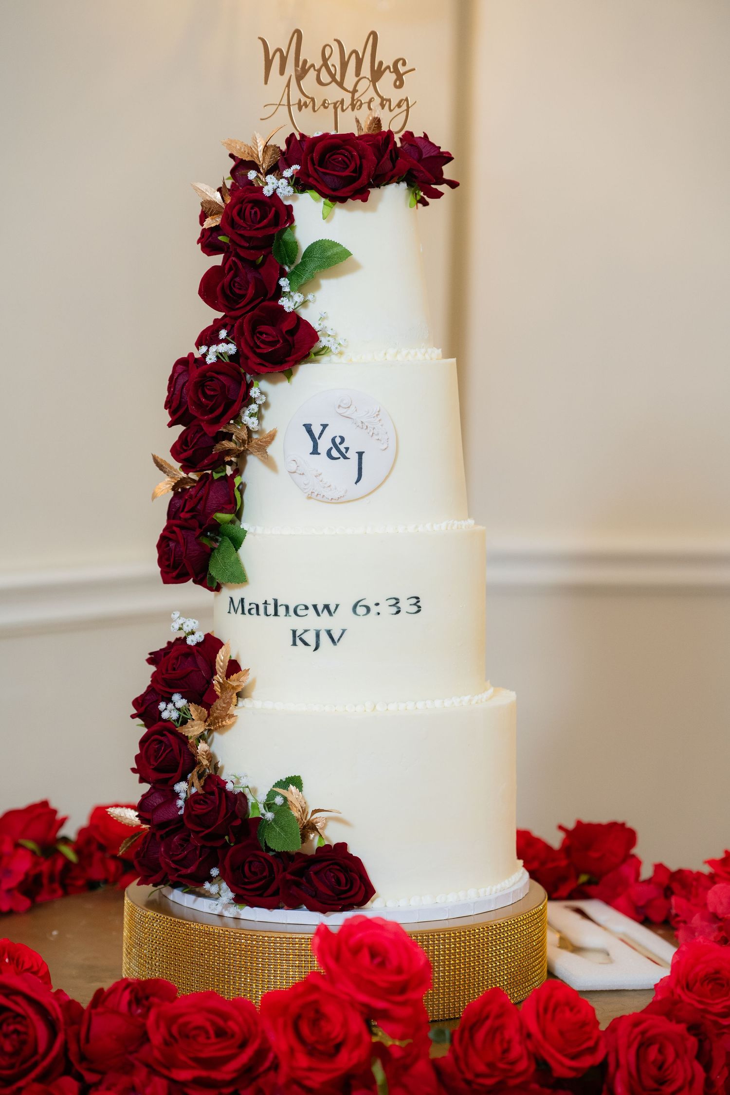 An elegant white wedding cake decorated with cascading deep red roses and gold accents.