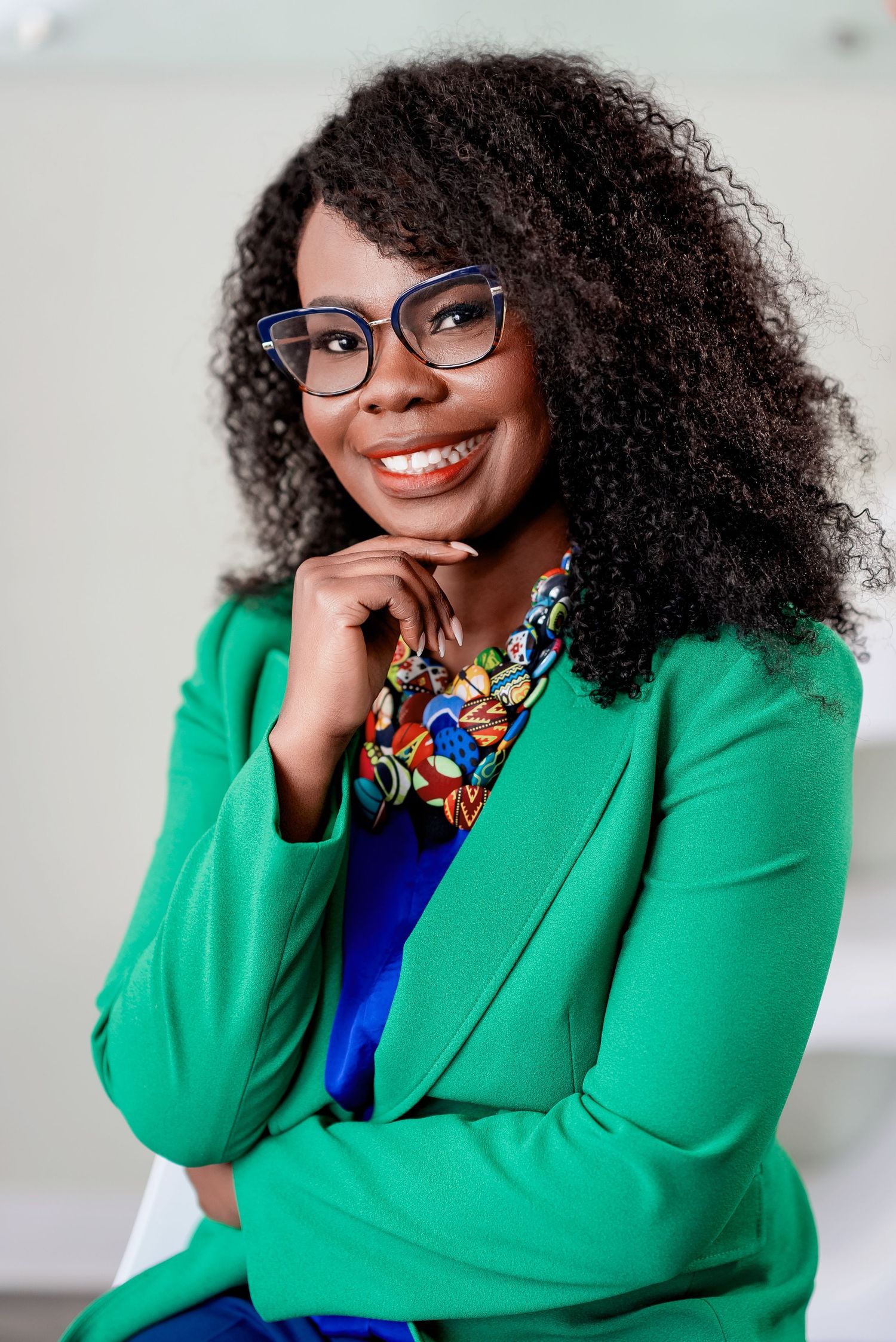 Professional portrait showing bright green blazer, stylish glasses, and colorful patterned blouse with natural curly hair.
