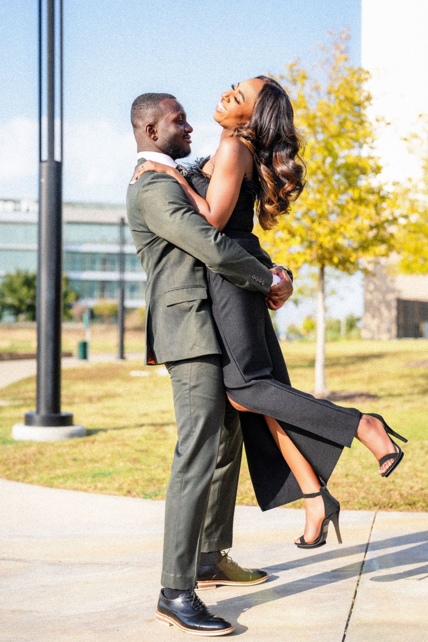 Playful couple in formal attire sharing a romantic lift moment outdoors.