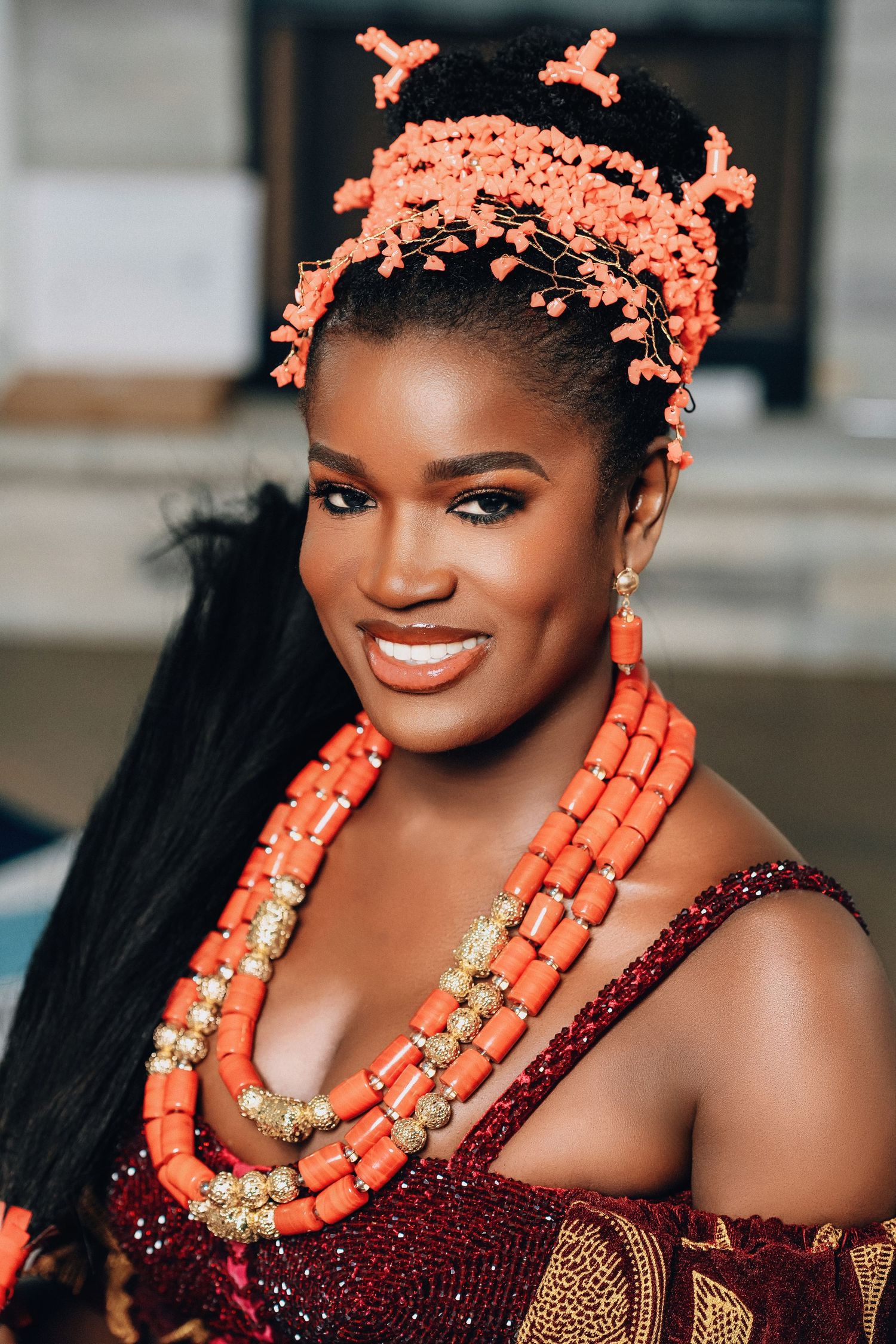Close up portrait showing coral beaded jewelry and traditional Nigerian bridal accessories against burgundy attire.