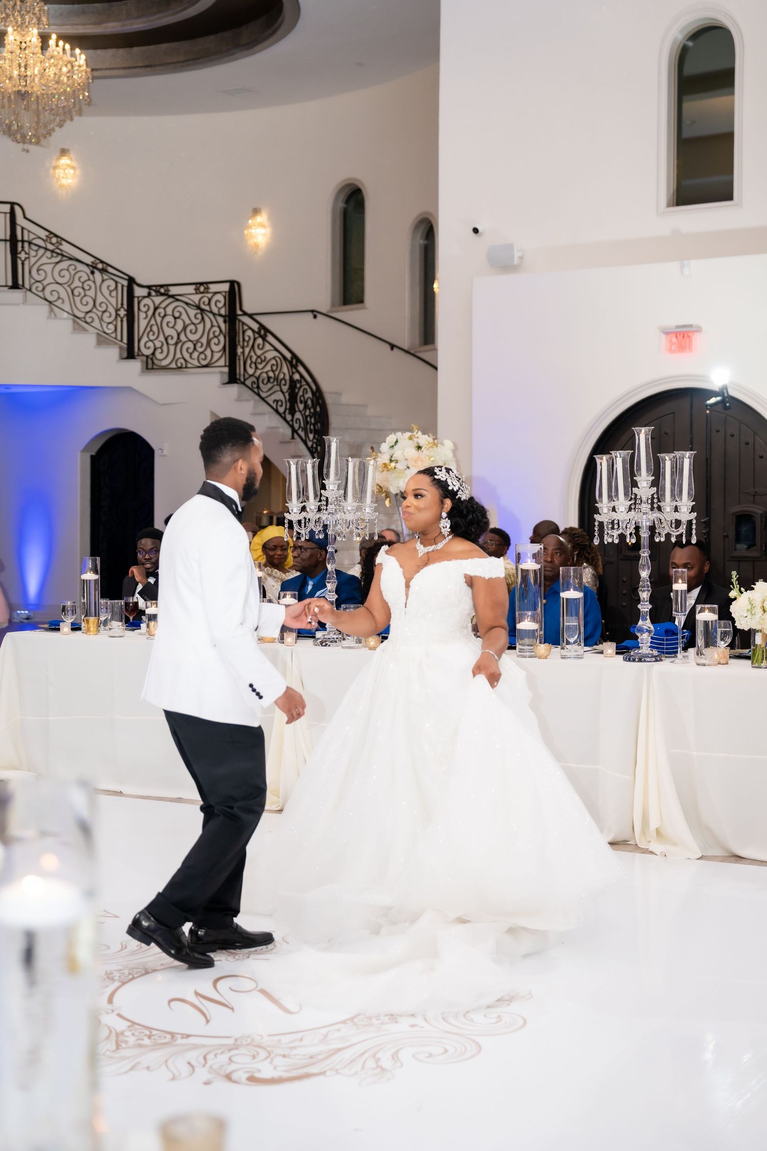 Elegant wedding reception venue with white decor, chandeliers, and romantic lighting.