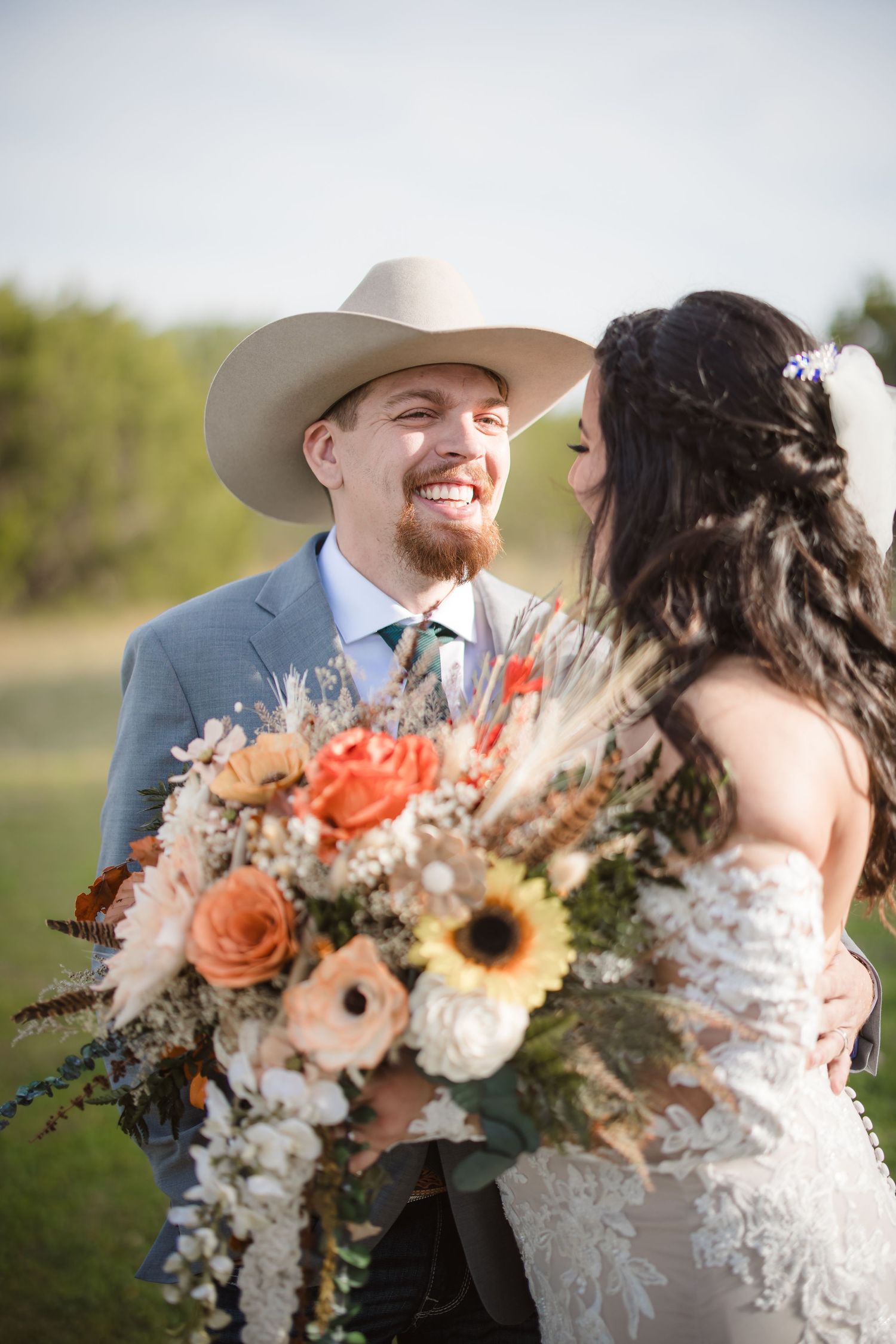 A joyful wedding moment outdoors with a beautiful bouquet featuring orange roses and sunflowers.