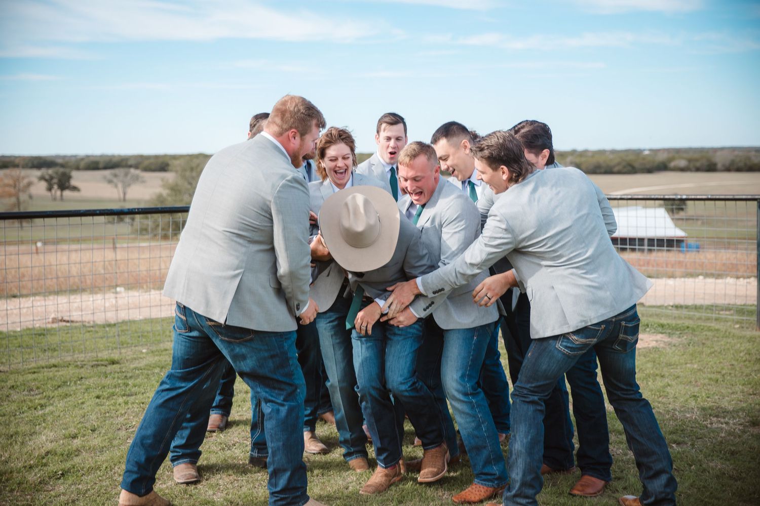 A candid moment of groomsmen huddling and laughing together on a grassy field.