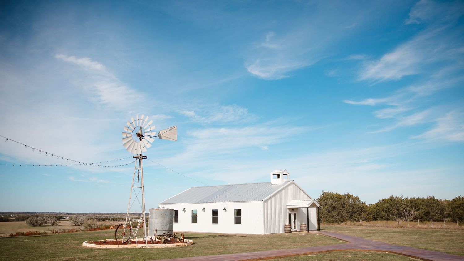 A white chapel with windmill against blue Texas sky in rustic countryside setting.