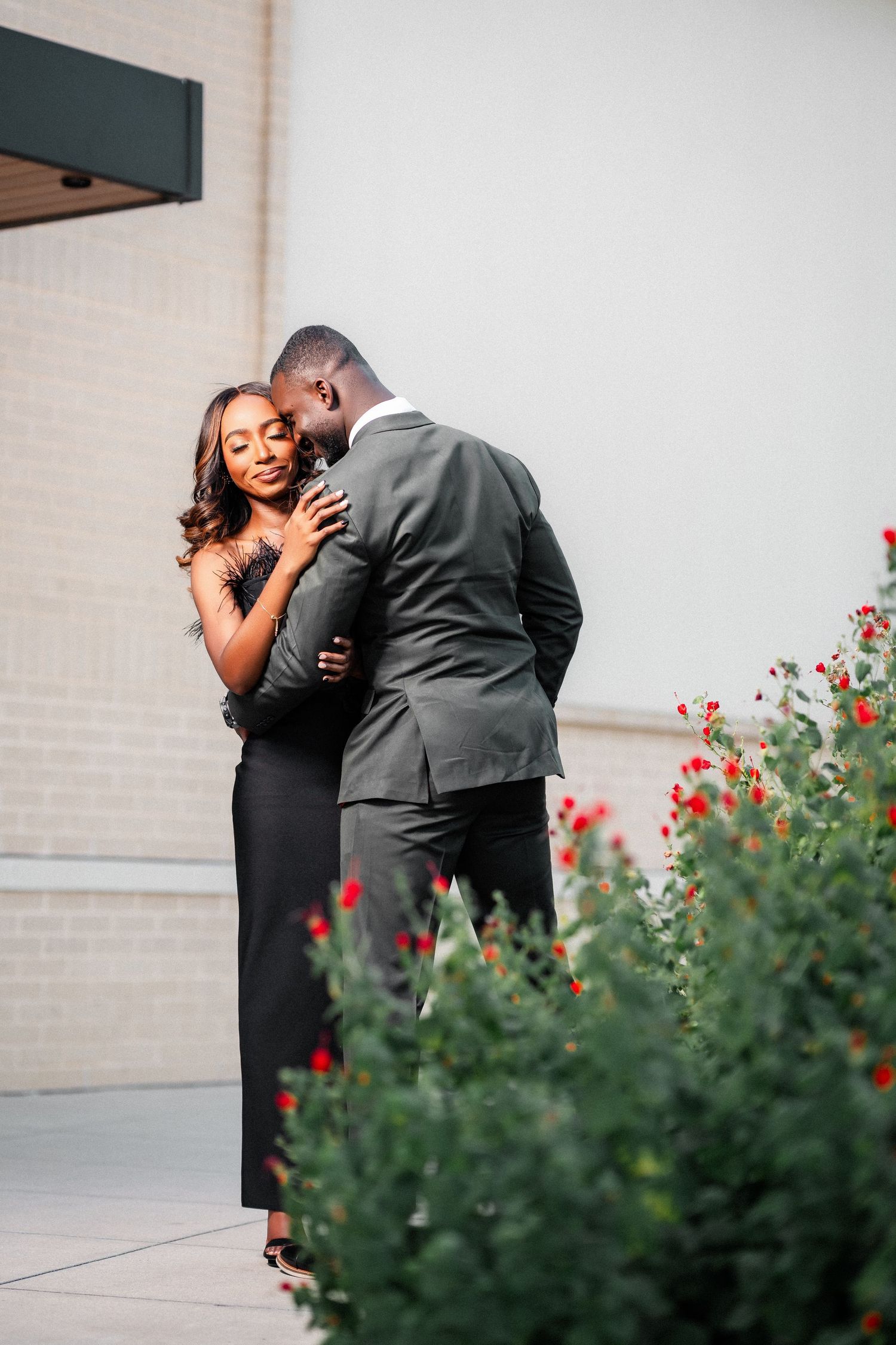Intimate moment captured between couple embracing near blooming red flowers.