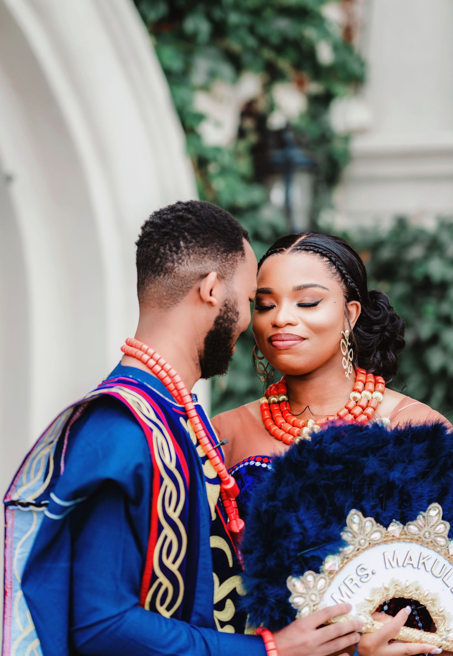 Wedding couple in blue and orange traditional attire share intimate moments against a white archway.