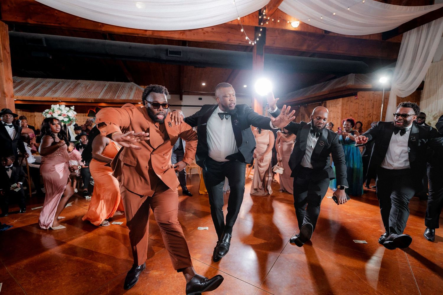 Wedding guests dancing and celebrating on a warmly lit reception dance floor.