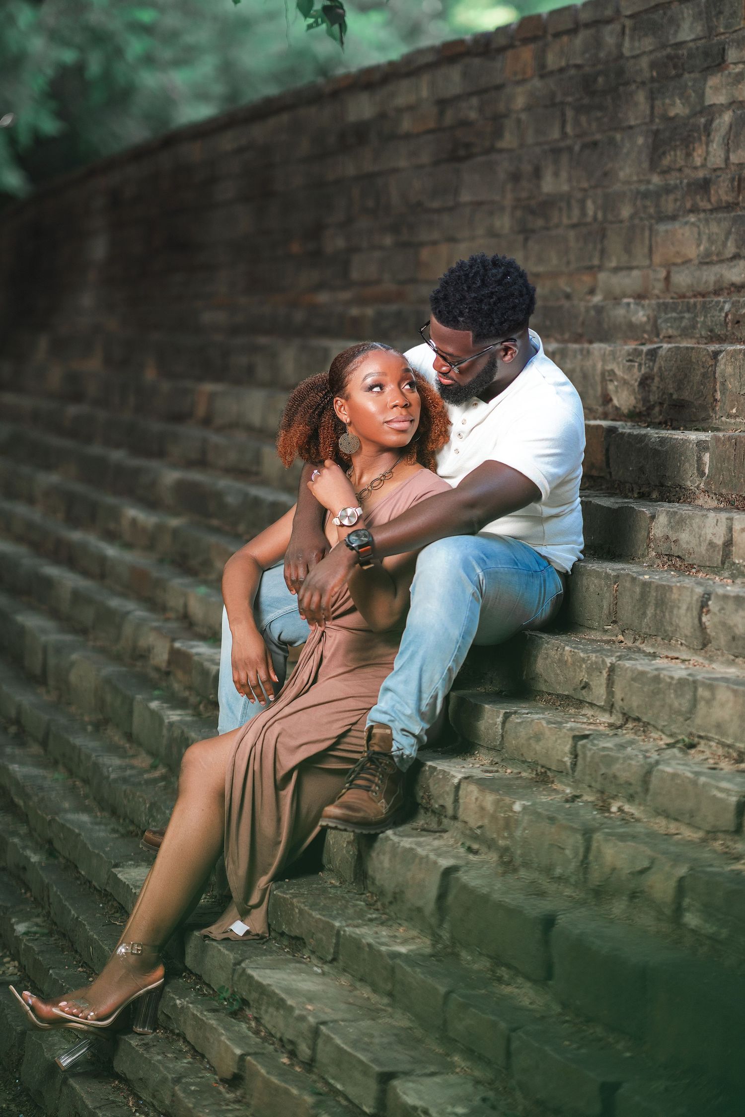 A couple sits romantically on brick steps outdoors during a golden hour photoshoot.