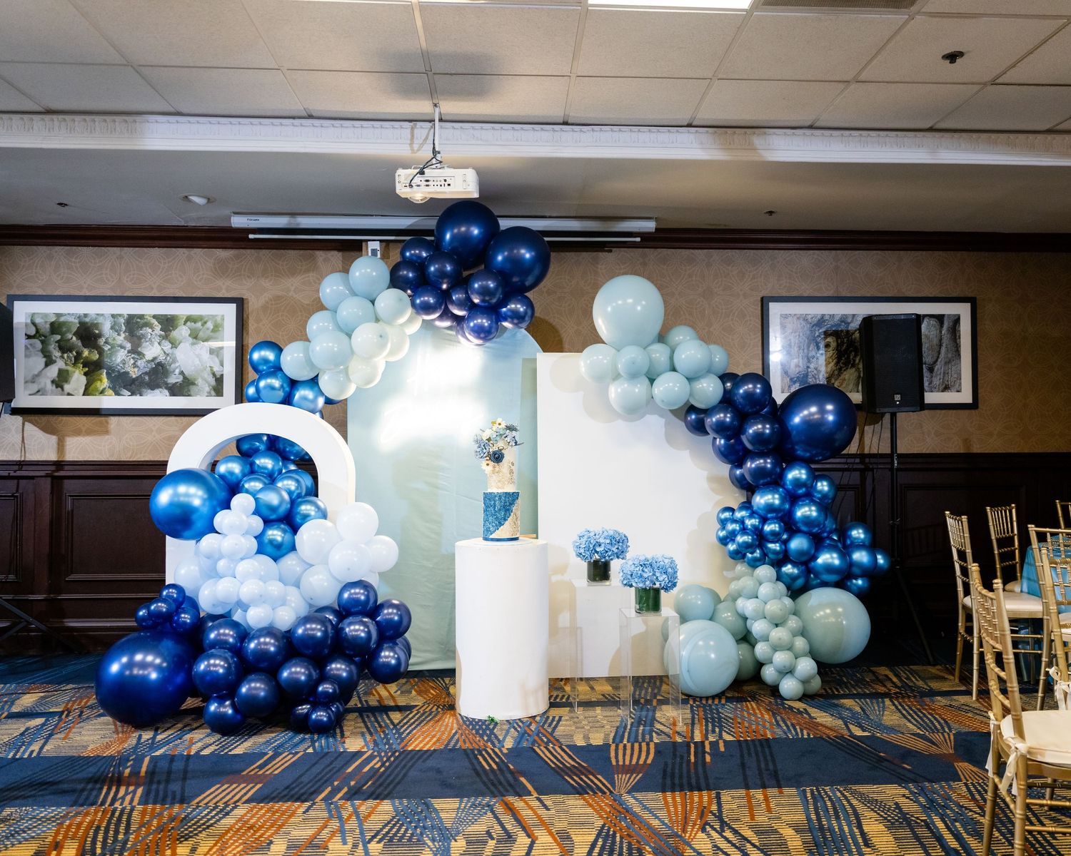 Blue and white balloon arch installation decorates a carpeted event space with modern lighting fixtures.