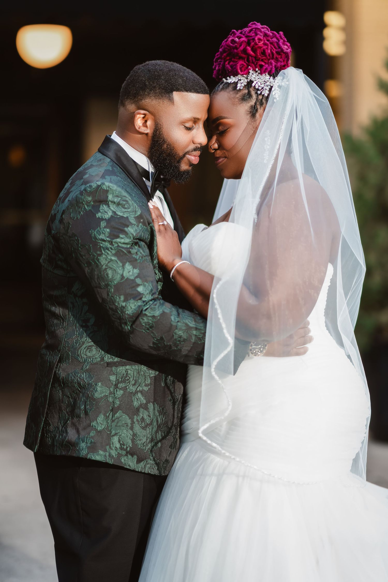 Wedding couple shares romantic moment in elegant attire with groom wearing emerald floral jacket.