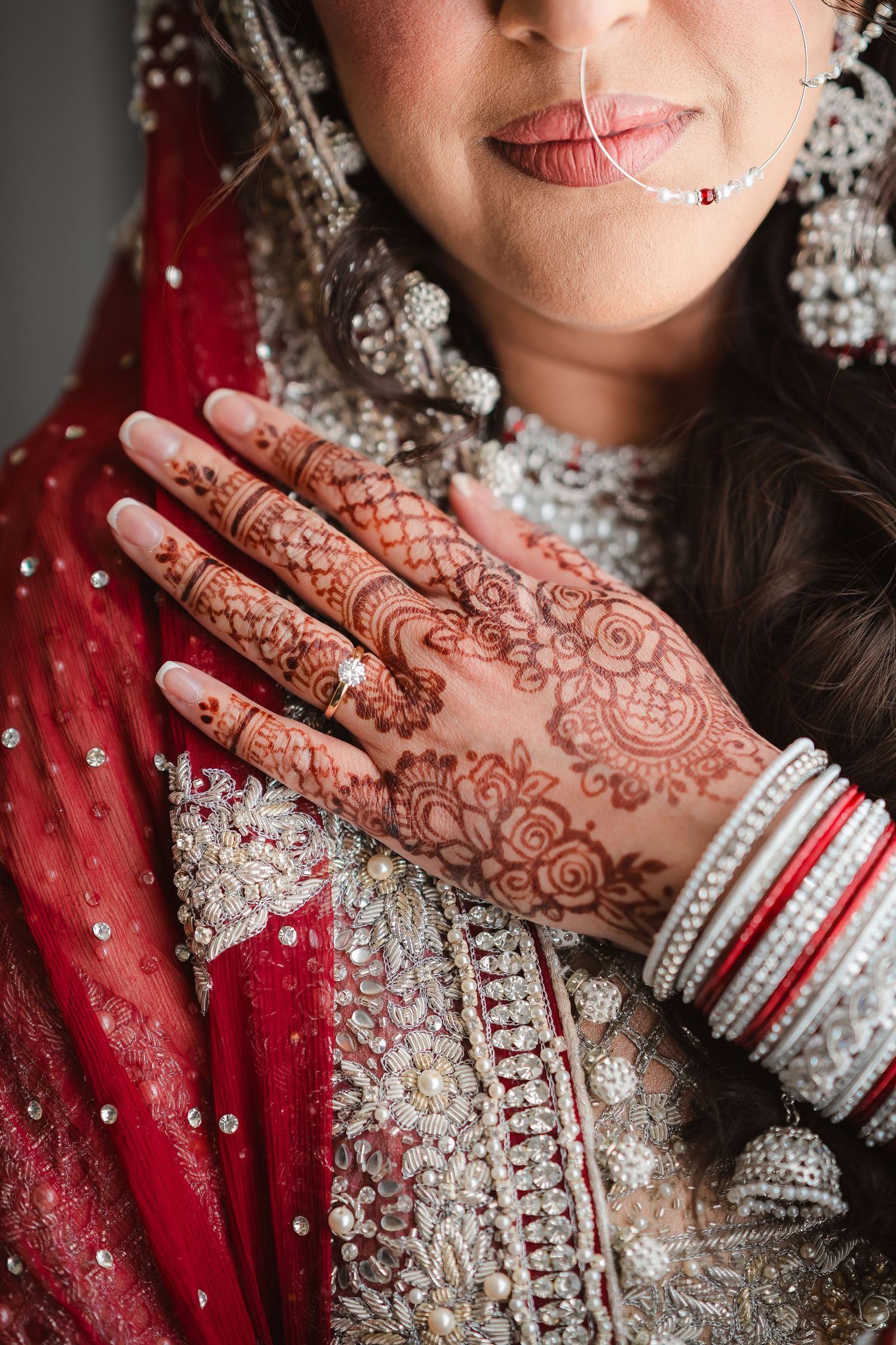 Close-up of intricate henna design on hand with red and silver traditional Indian bridal attire and jewelry.