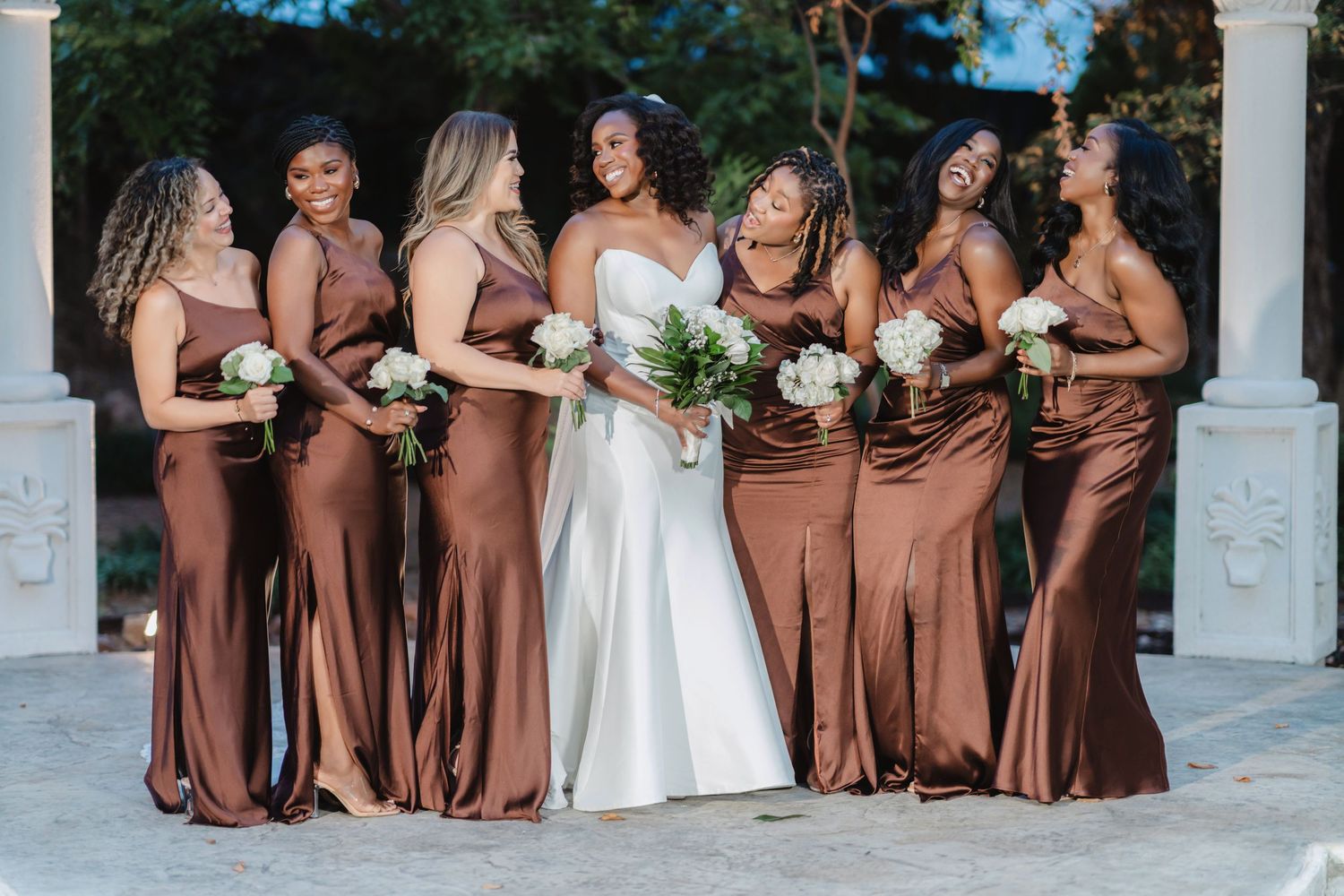 Wedding party poses in coordinated brown and white attire on outdoor steps.