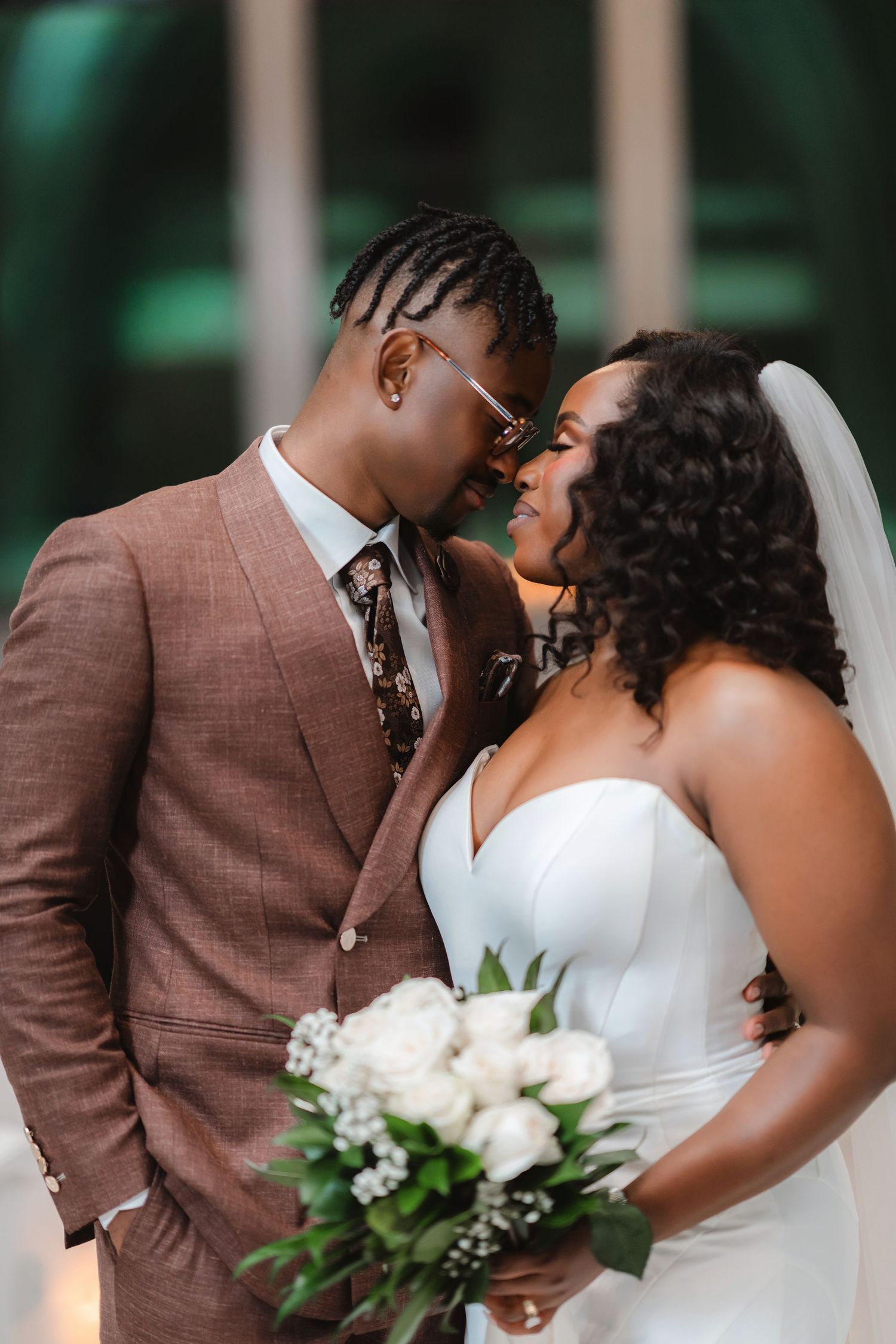 A romantic wedding couple shares an intimate kiss in front of a blurred green background.