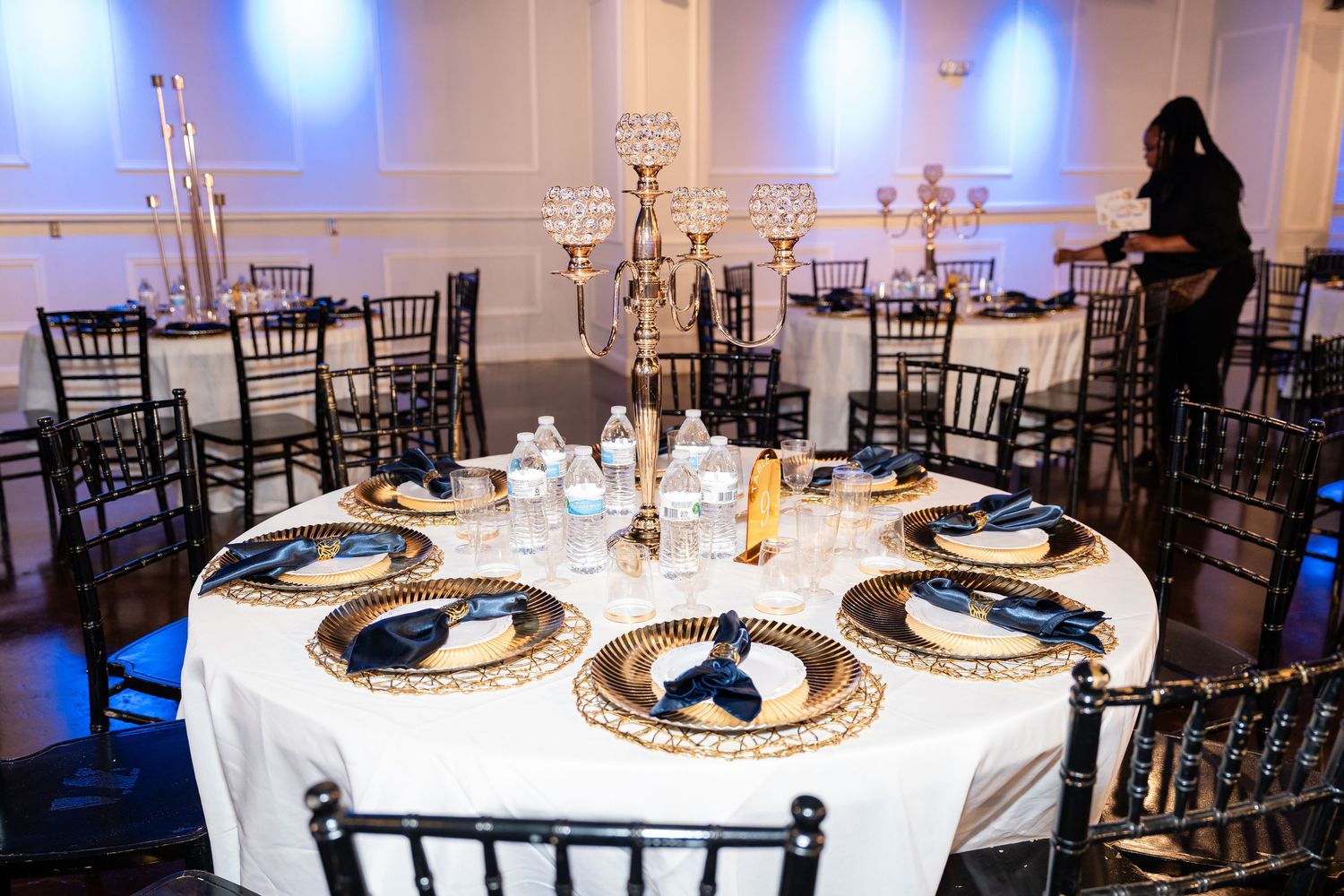 Elegant wedding reception tables with navy and gold place settings and black chiavari chairs.