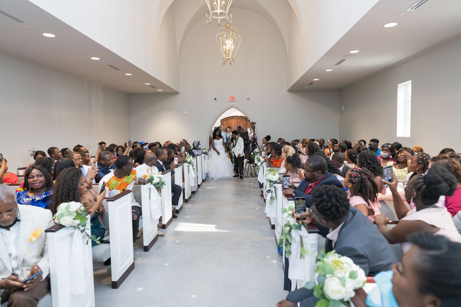 Large group seated in rows along a white hallway corridor during an indoor gathering.