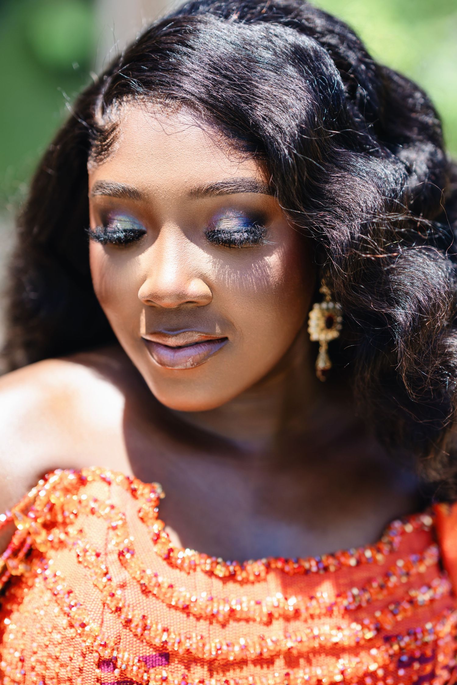 Close-up beauty shot showcasing sparkly orange sequined dress details and glamorous makeup.