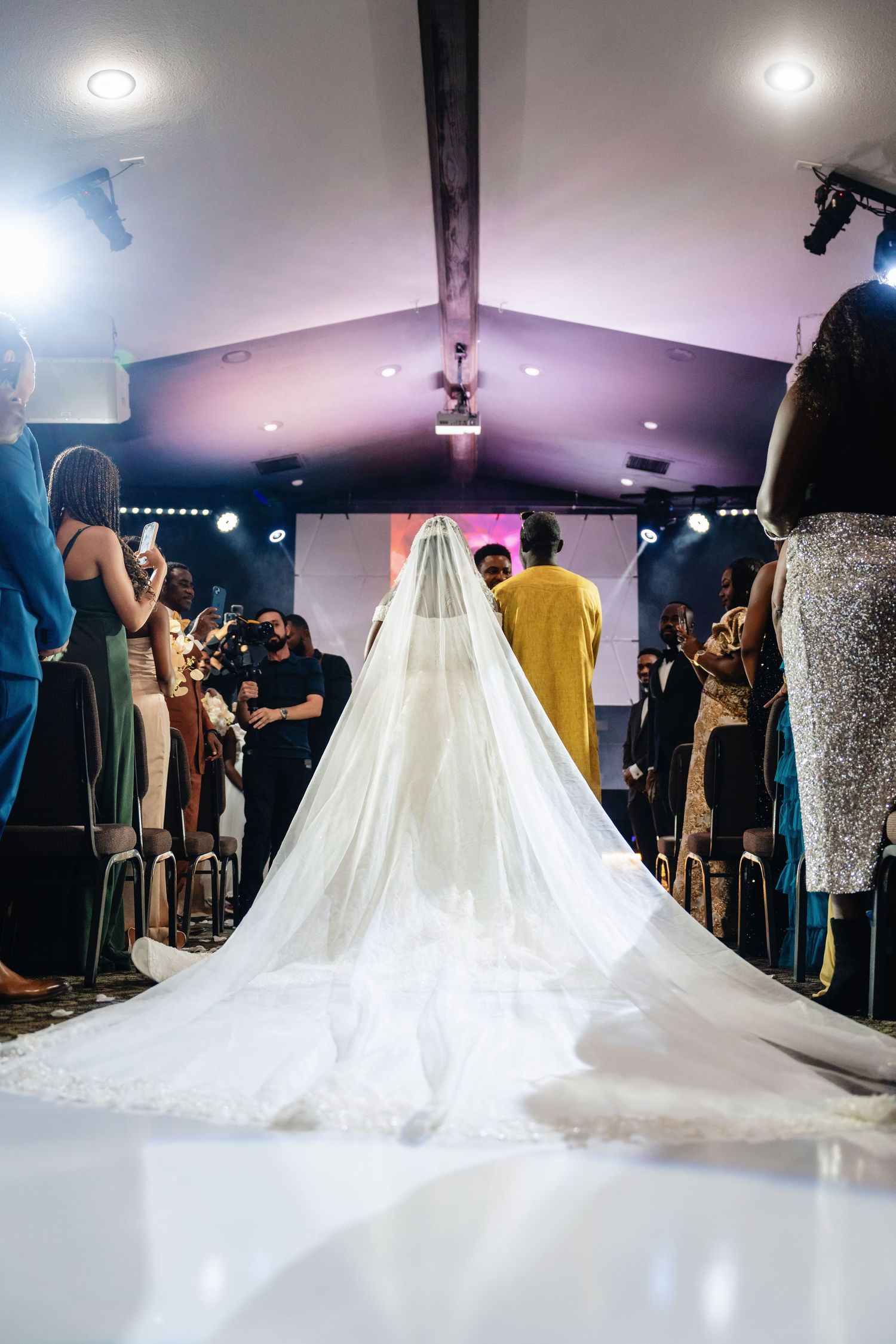 Dramatic cathedral-length wedding dress train flowing across ballroom floor with guests in background.