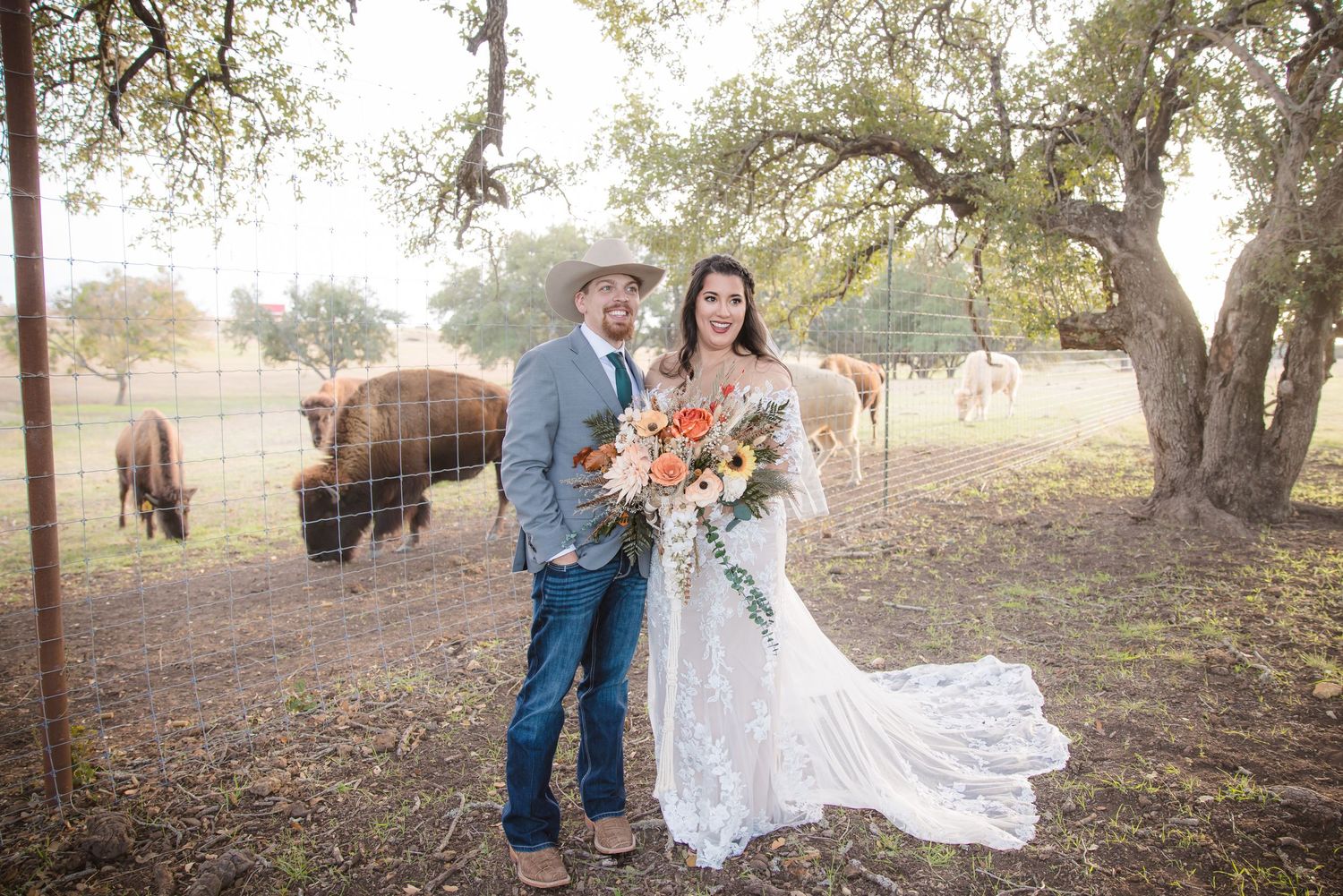 A couple poses together outdoors under oak trees on a sunny autumn day.