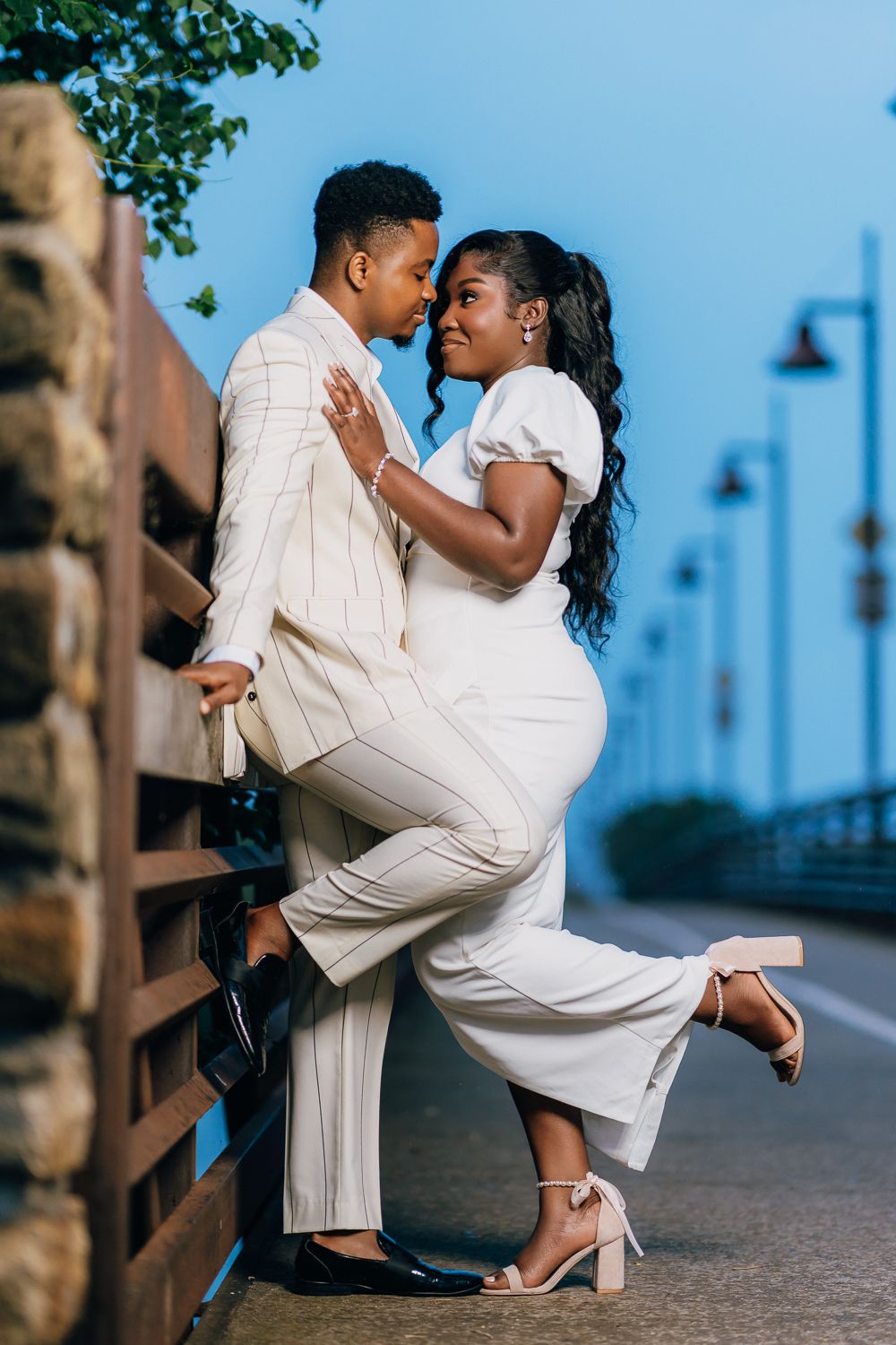 A couple in matching white outfits strikes a romantic dance pose on a boardwalk.