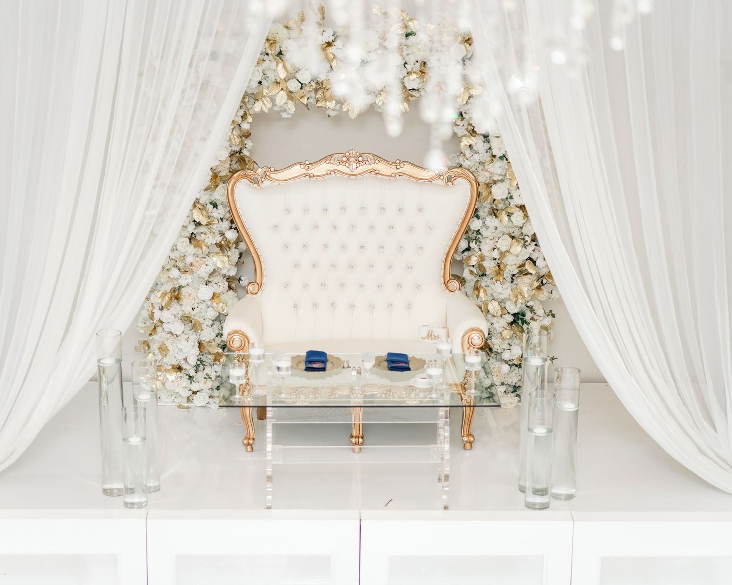 Elegant white and gold wedding reception decor with crystal chandeliers and draped fabric creating a luxurious ambiance.