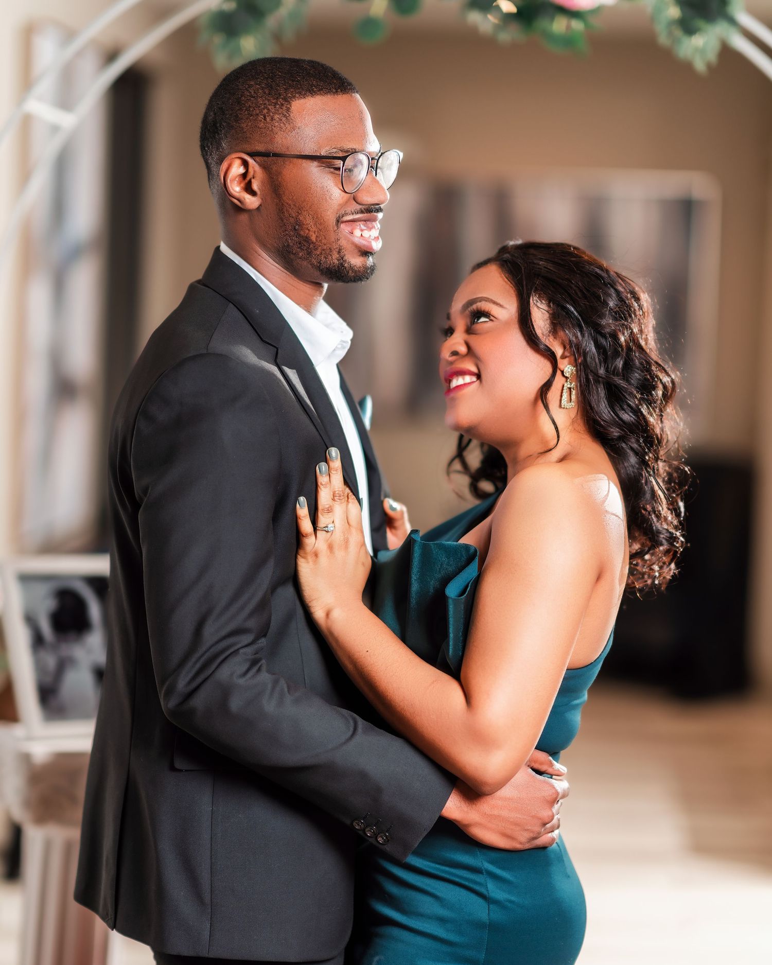 A couple embraces while laughing together, with one wearing a teal dress and the other in a dark suit.