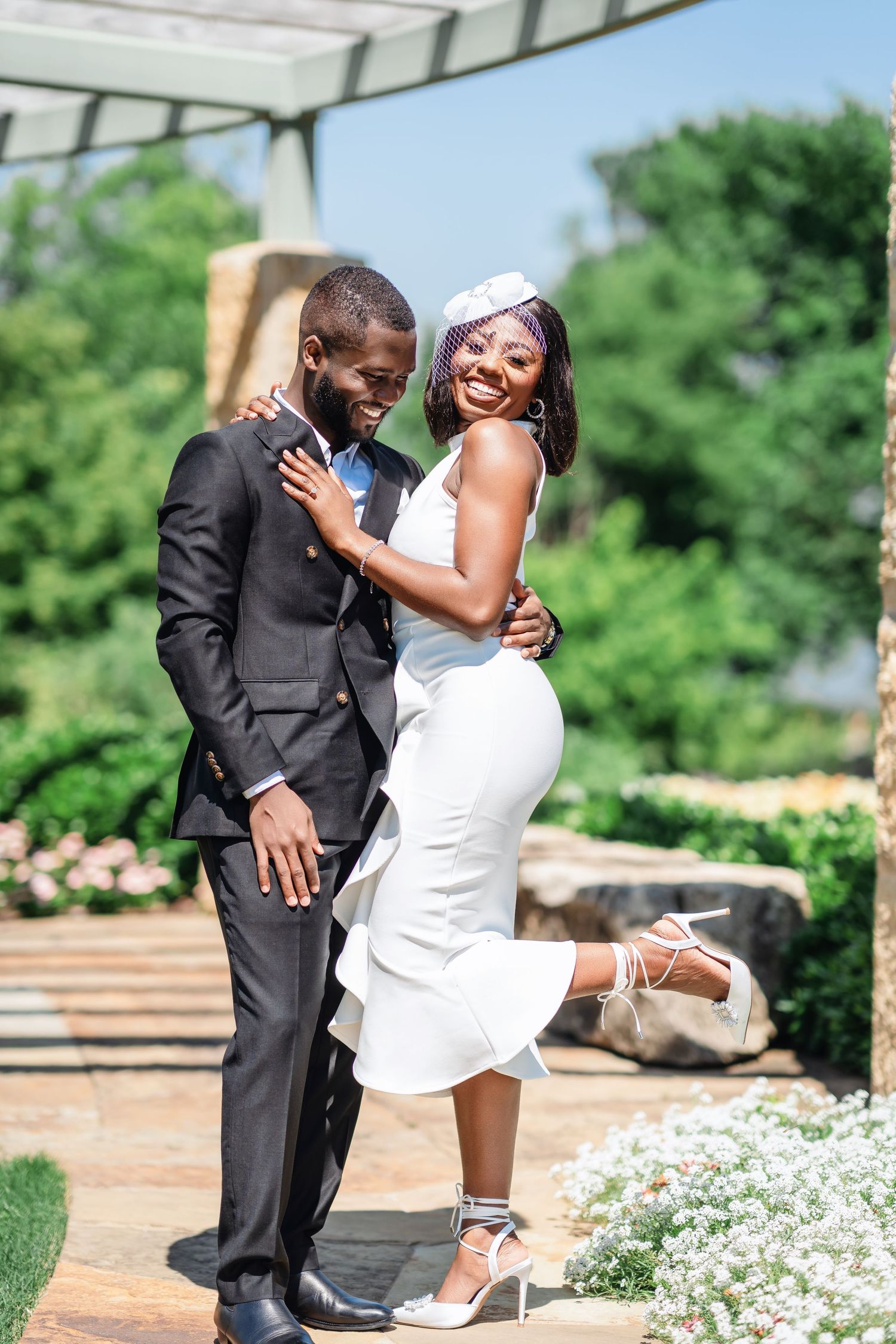 A couple shares a romantic dance move on a garden pathway surrounded by blooming flowers.