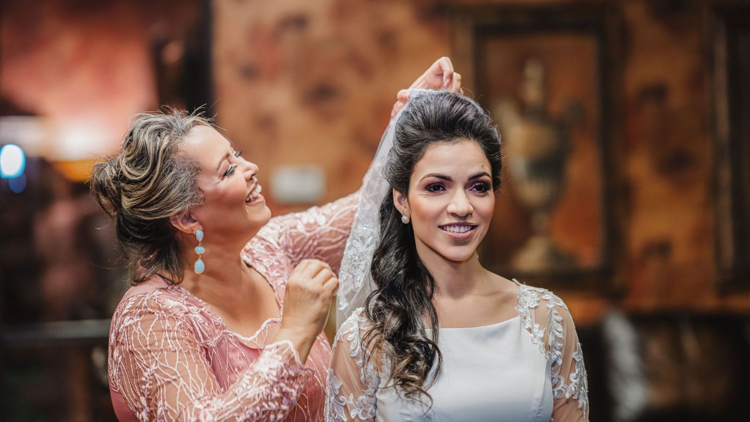 Two women share a joyful moment while preparing for a wedding celebration.