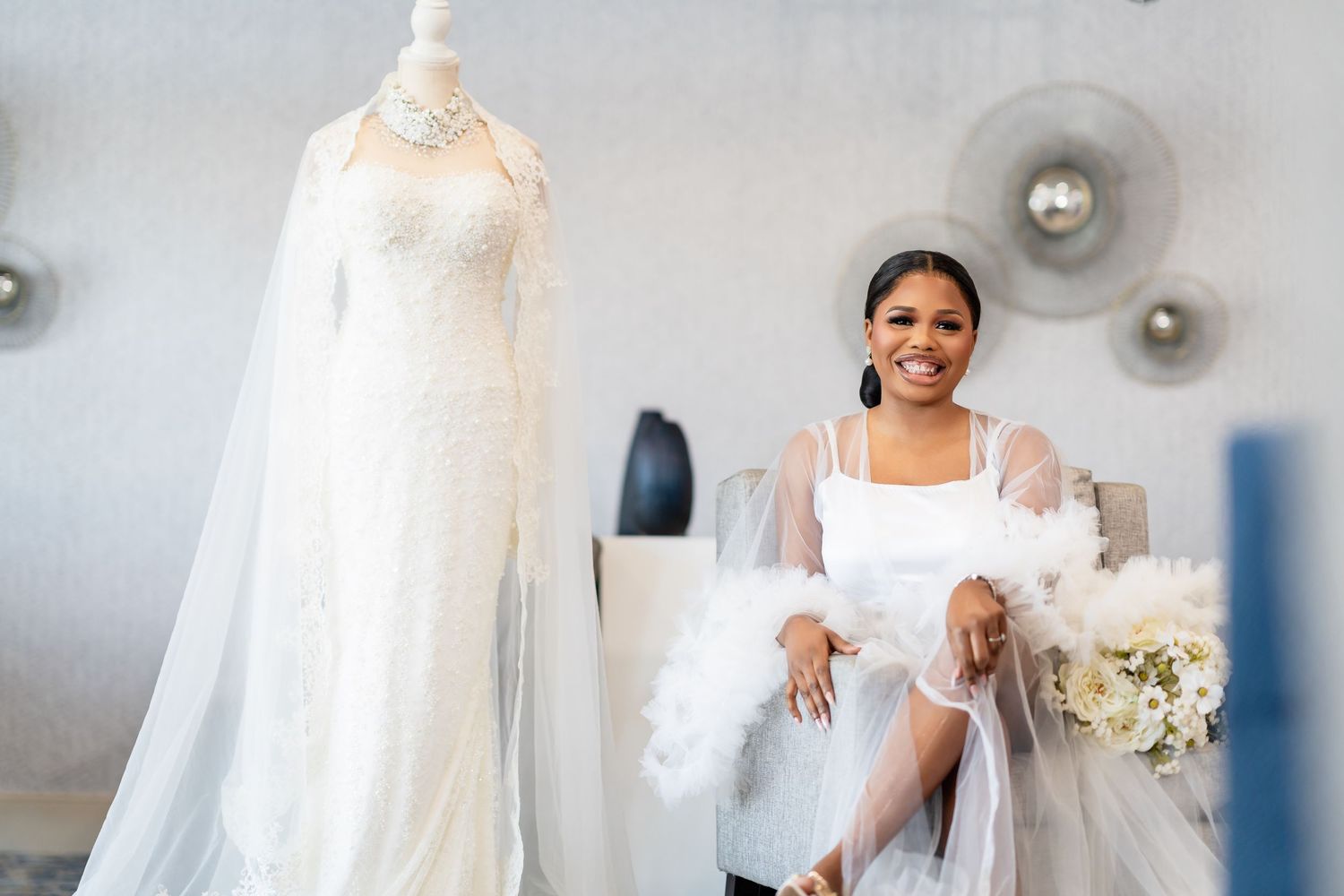 Bride in elegant white wedding dress posing against light background with decorative silver spheres.