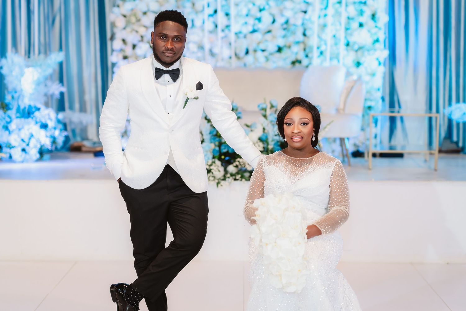 A joyful couple poses together at their elegant winter wedding with blue and white decor and floral arrangements.