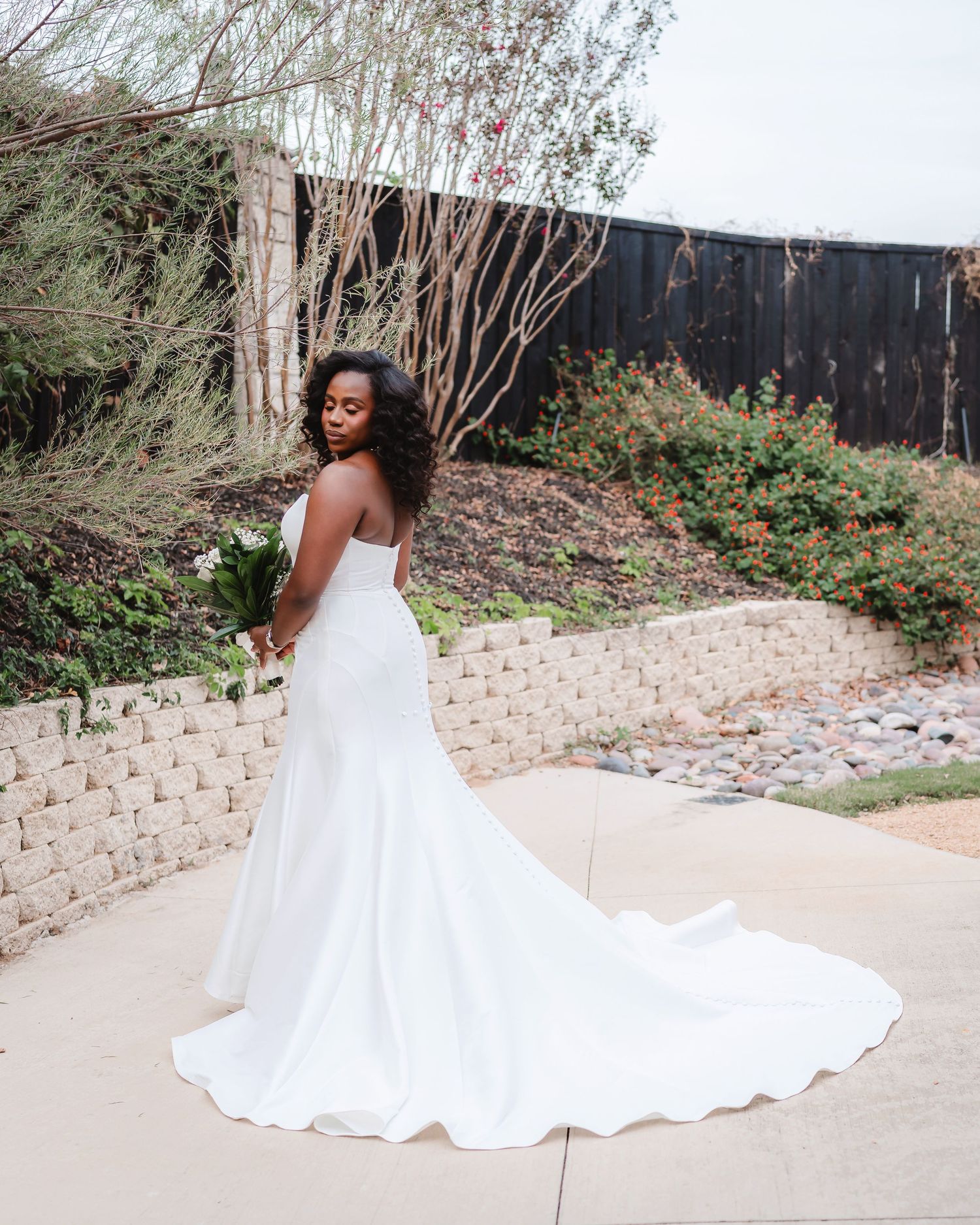 A stunning white wedding gown with a flowing train is showcased against a landscaped garden backdrop.