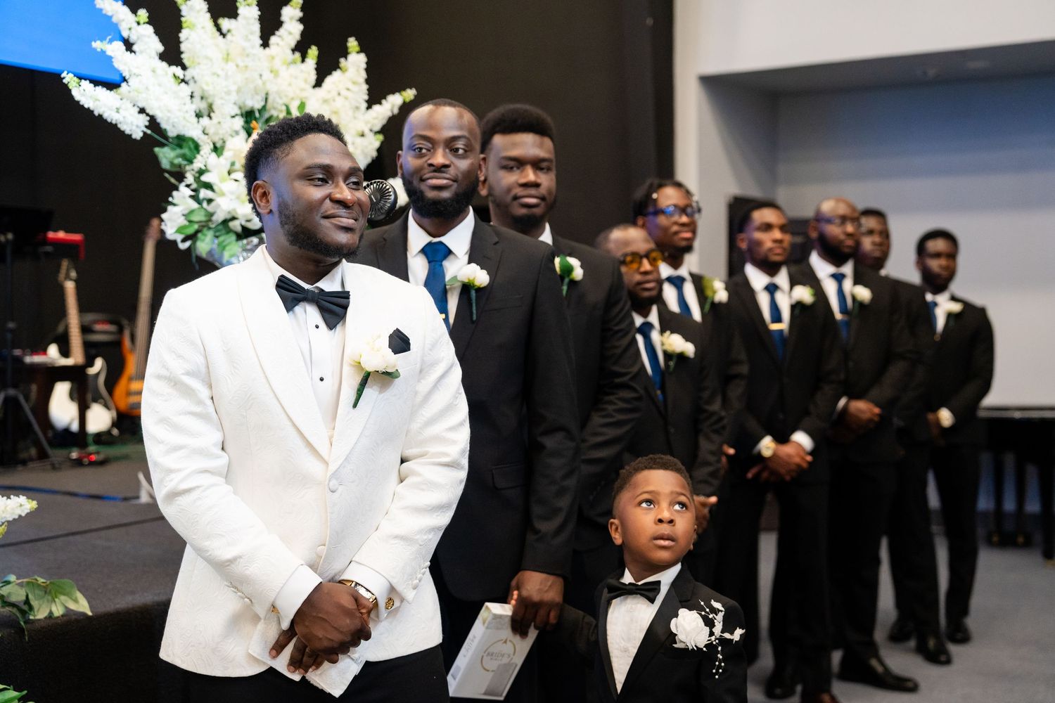 Groomsmen in black tuxedos and white jackets gather for formal wedding party photos.
