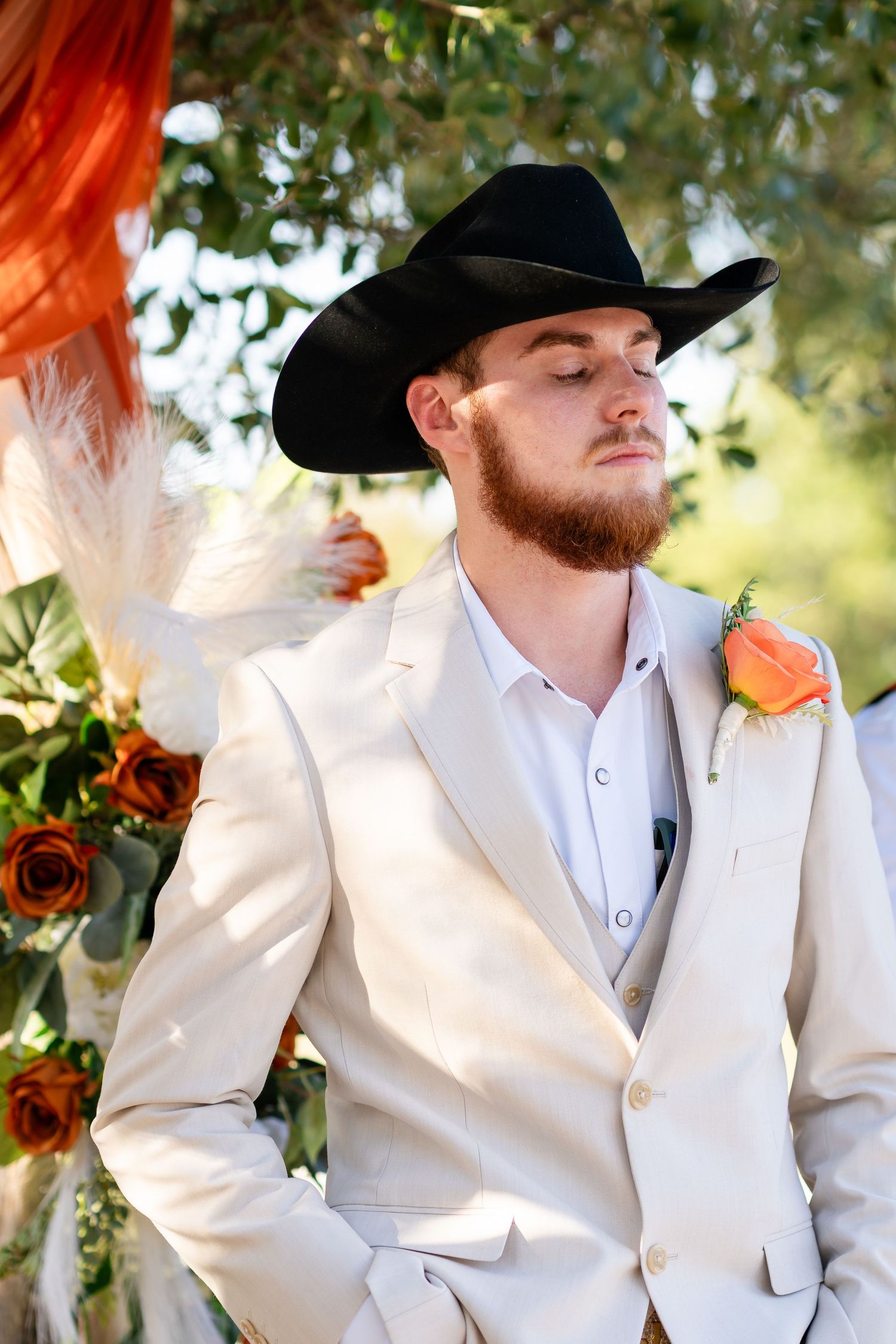 Groom in white blazer and black cowboy hat with coral boutonniere.