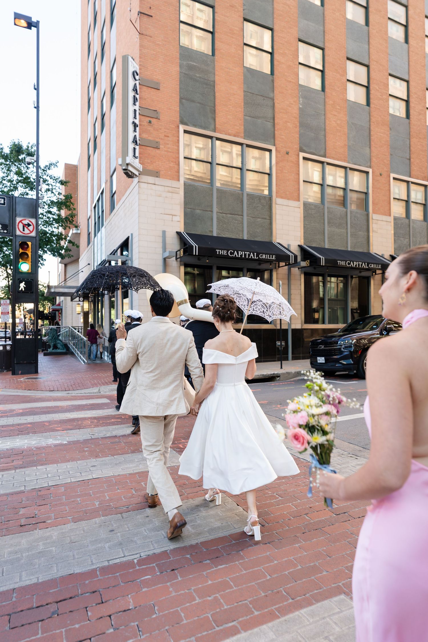 A couple walks down a brick sidewalk outside The Capital Grille restaurant on a sunny day in the city.