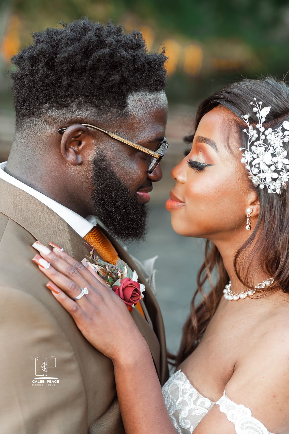 A romantic wedding portrait showing a tender moment between newlyweds in brown suit and white dress with floral accessories.