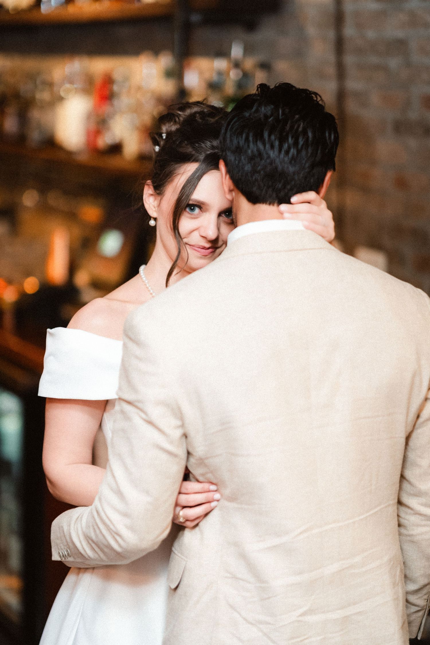 A couple shares an intimate moment in formal attire against a rustic brick wall background.