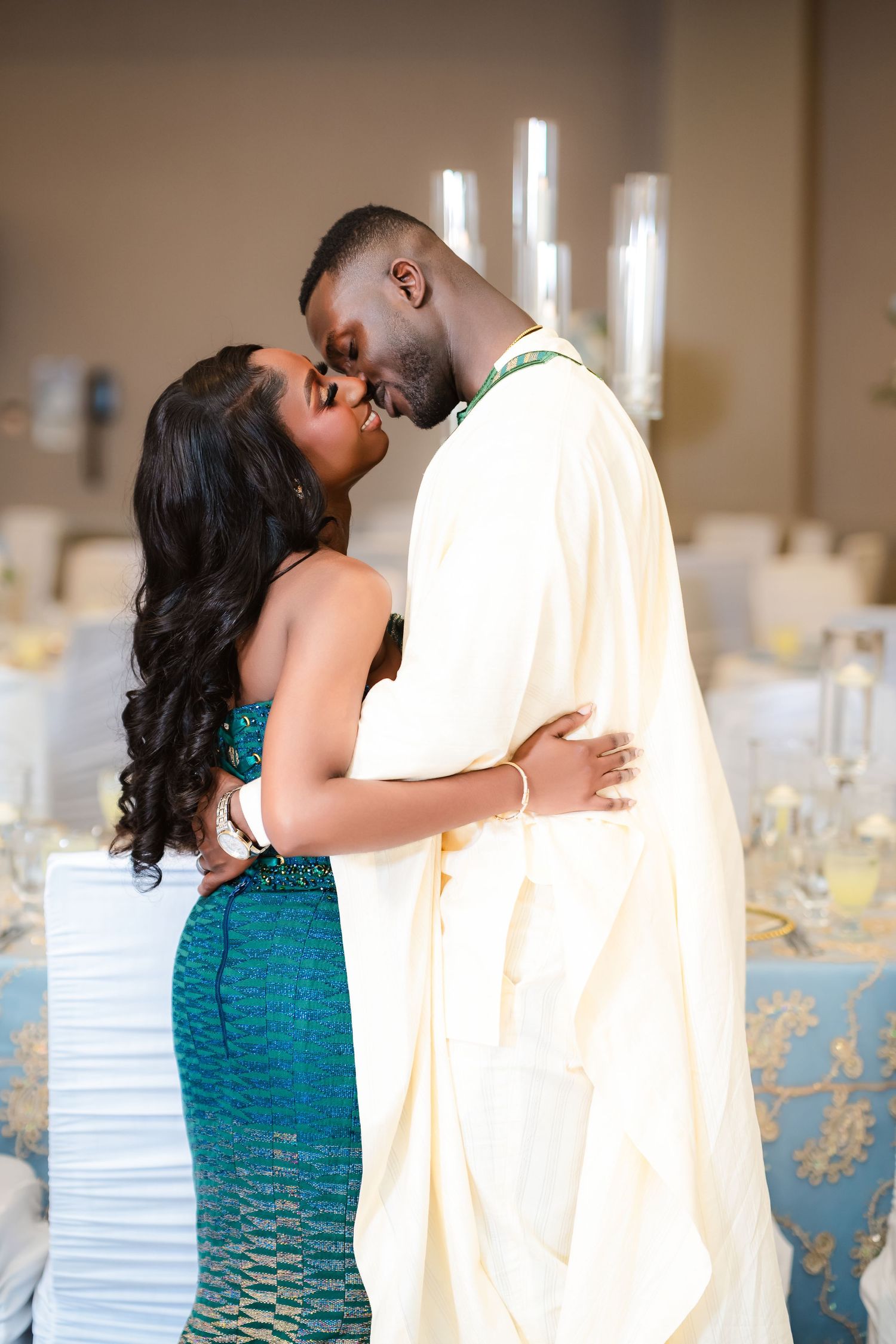 A couple shares an intimate moment at their wedding reception, with the bride in a teal dress and groom in white attire.