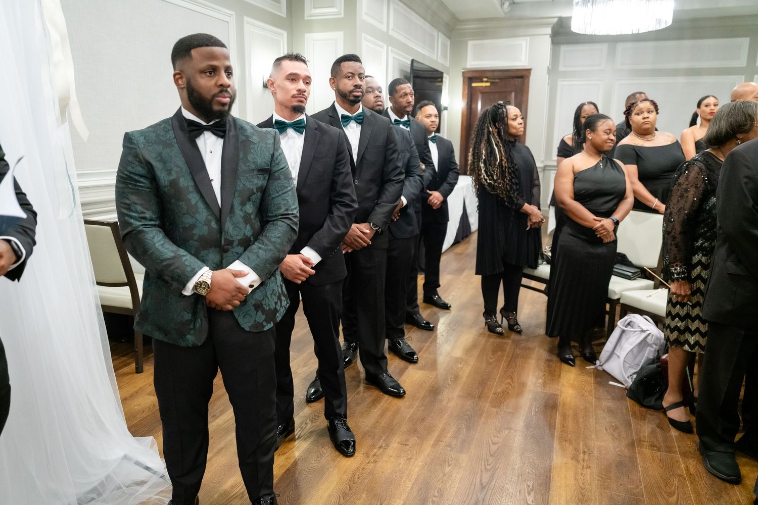 Wedding party members dance and celebrate together on a polished wooden dance floor at an indoor reception.